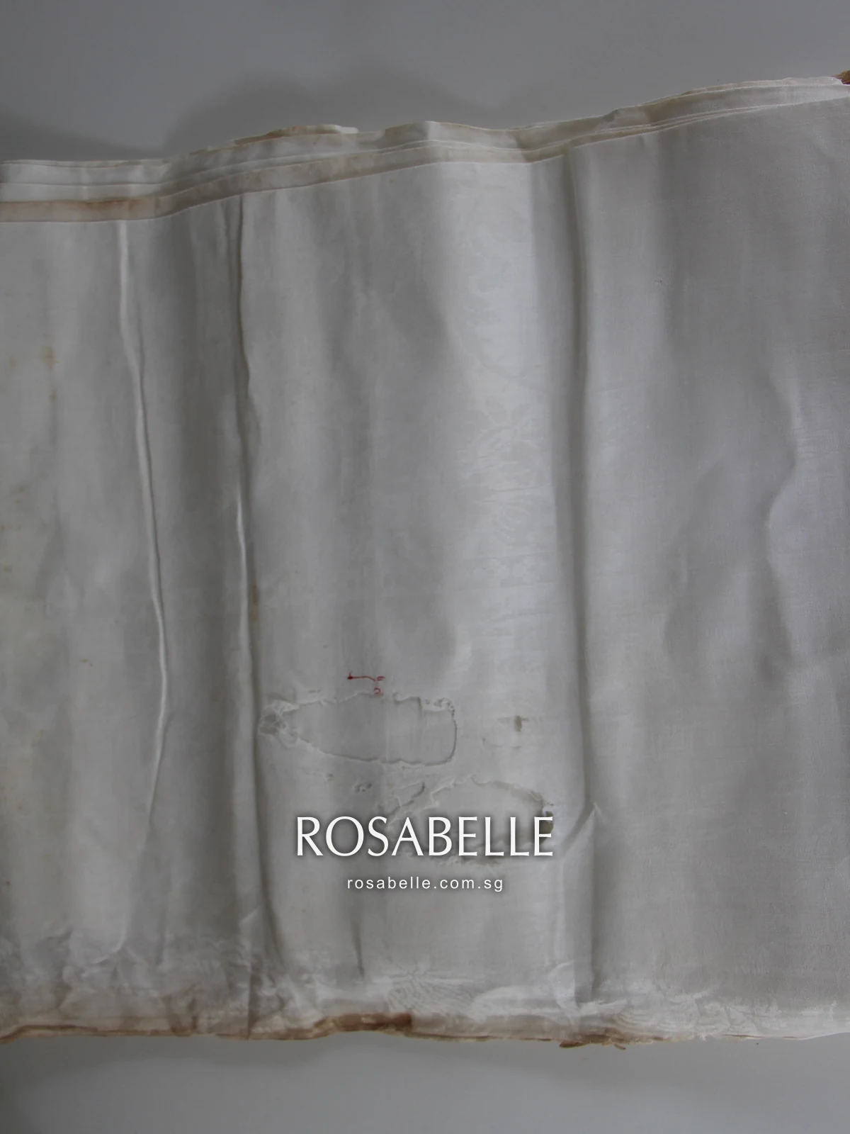 Folded antique linen hung on a rail, rust-brown staining along each folded edge where it was stored