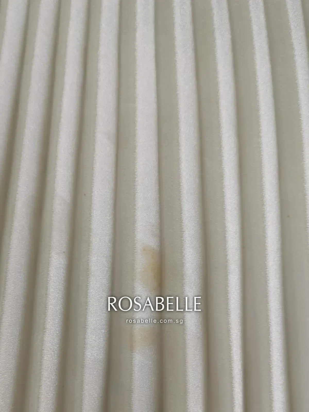 Close-up of yellow marks sitting inside the folds of a cream pleated skirt