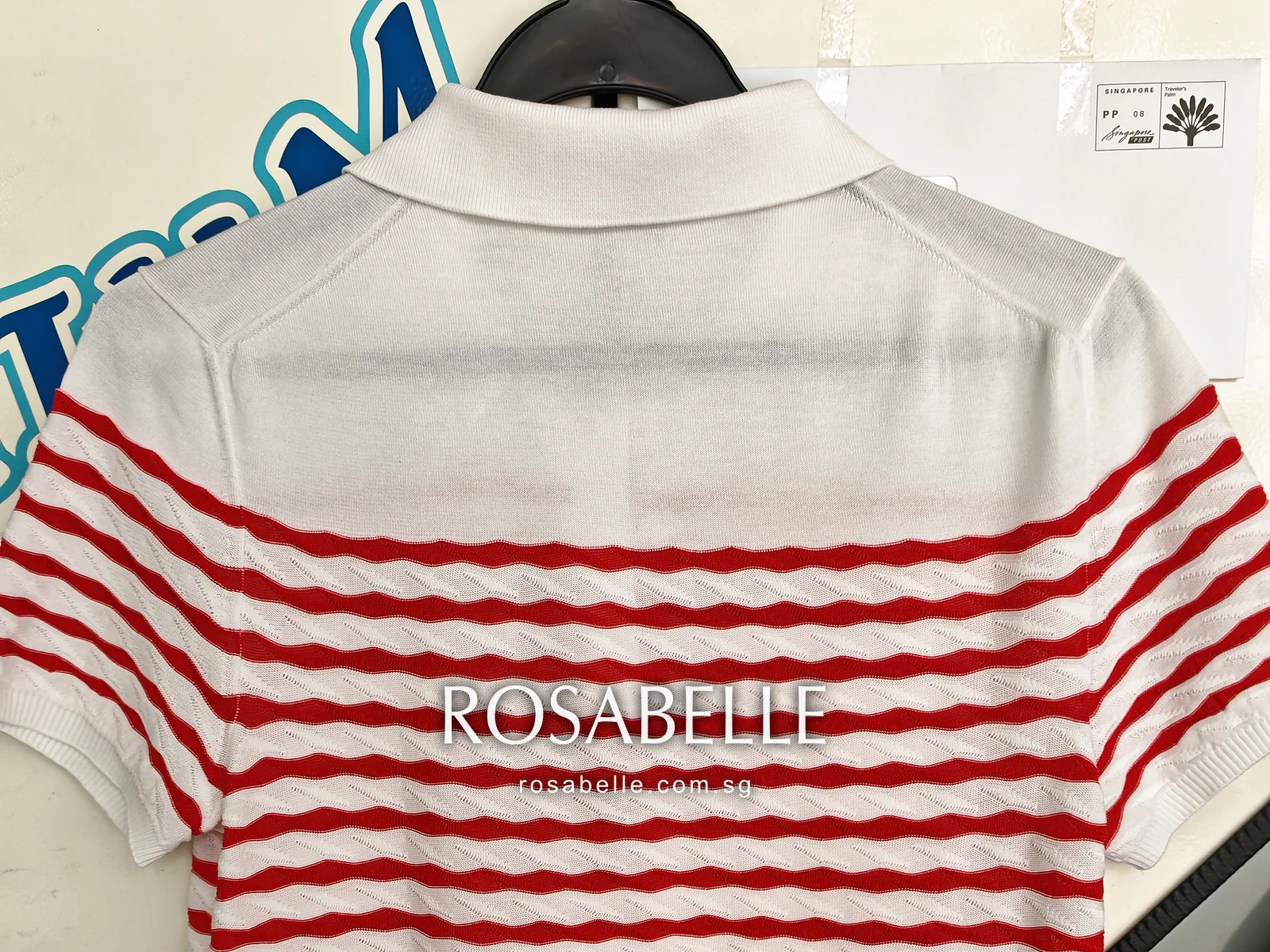Back of the same polo on a hanger after cleaning, the white knit below the collar clear above the red wavy stripes