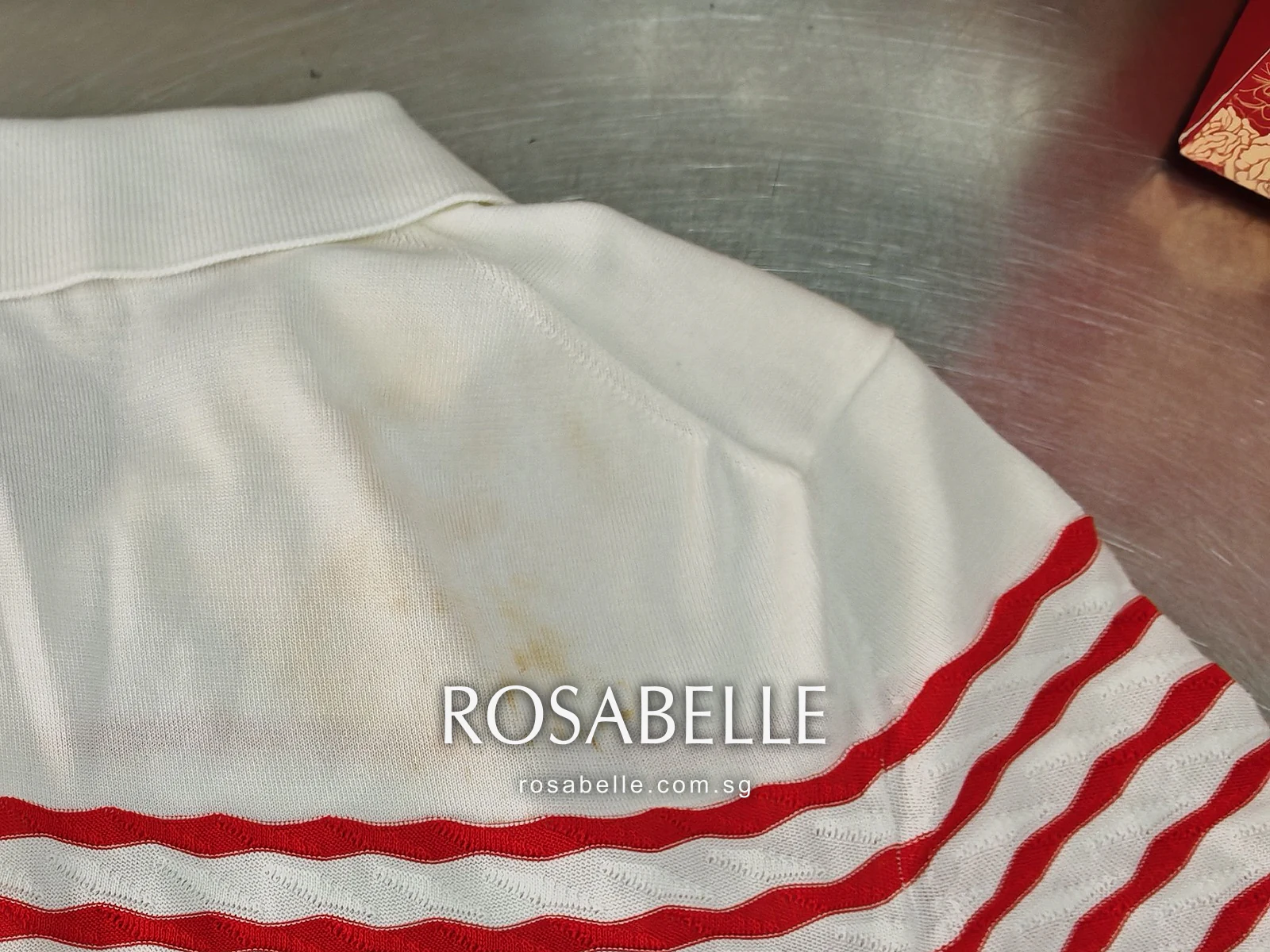 Close view of the polo's right back shoulder below the collar, a cluster of yellow spots on the white knit above the red stripes