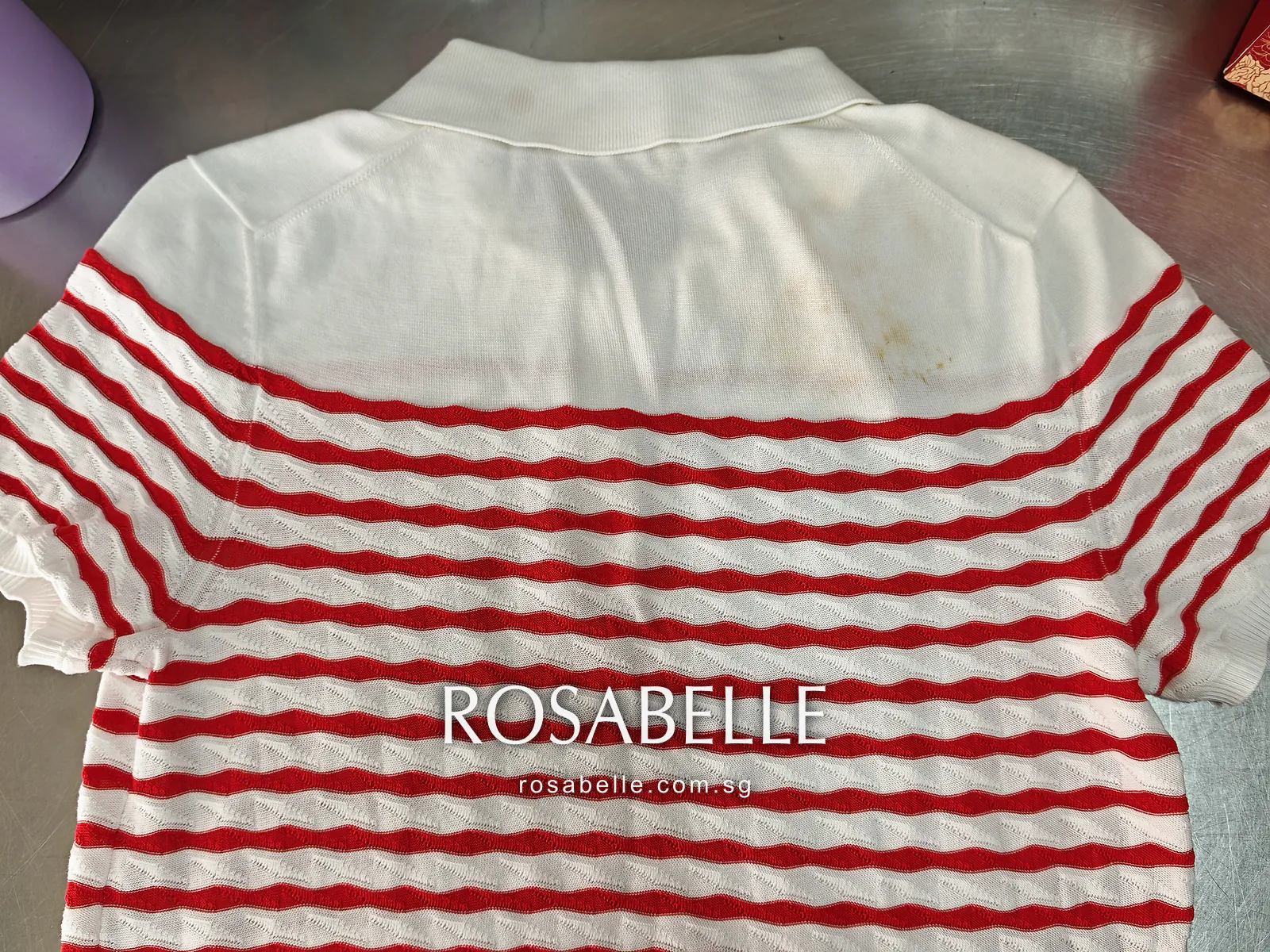 Back of the white and red striped Chanel knit polo laid flat, yellow spots on the white knit near the right shoulder