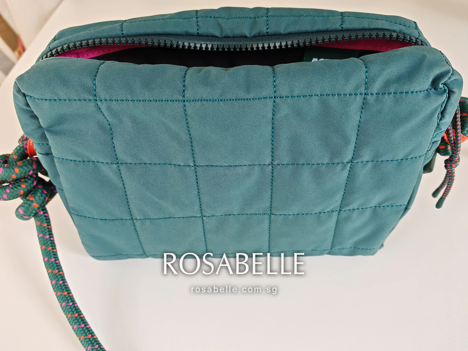 Back of the teal bag after cleaning, seen at an angle with the pink lining showing at the zip