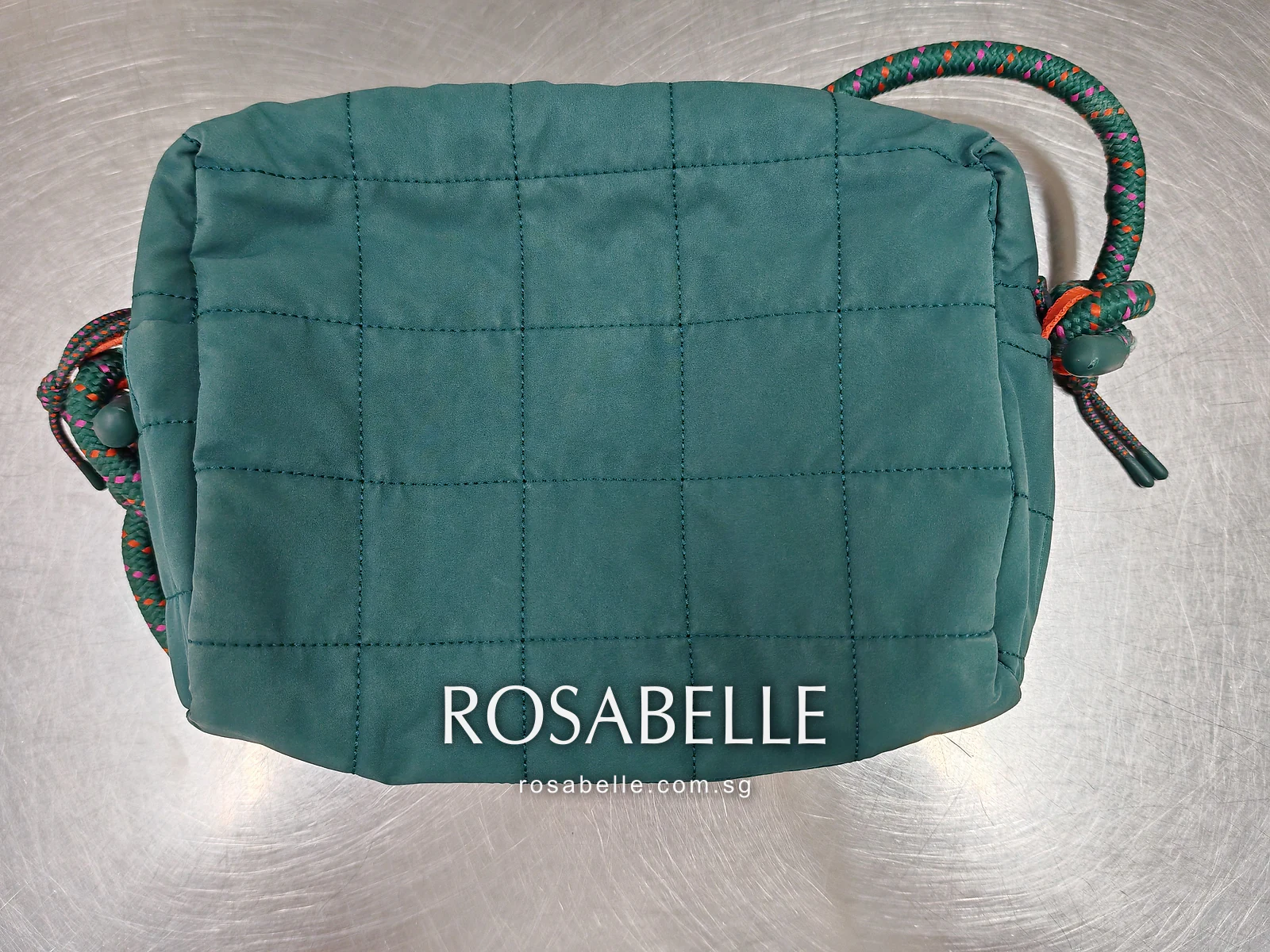 Back of the teal quilted bag on the steel bench, rope strap knotted at one side, before cleaning