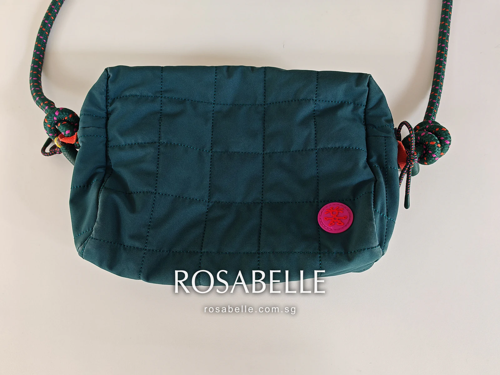 The same teal quilted bag after cleaning on a white table, its rope strap looped above and the pink badge at the corner