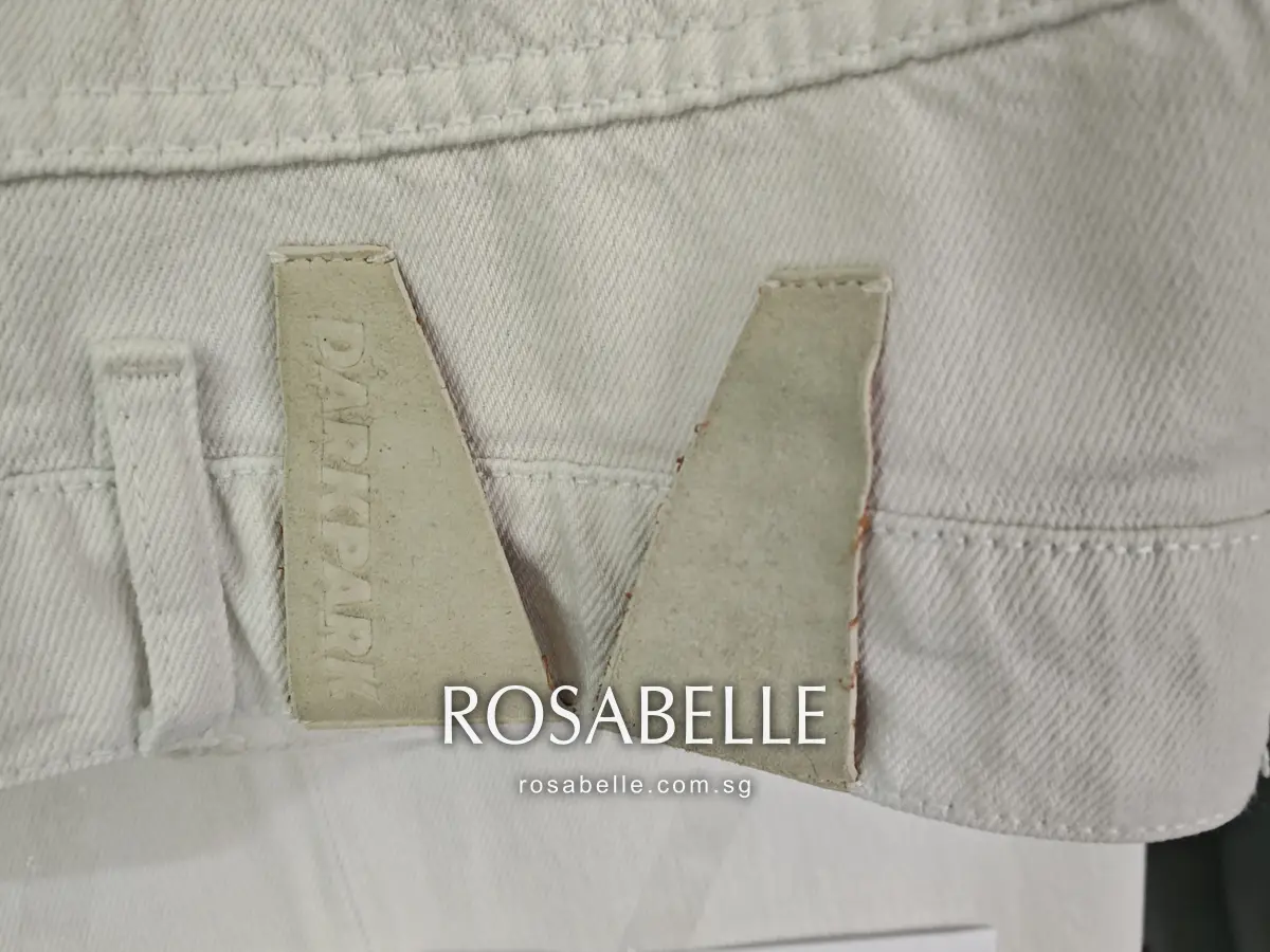 Two-piece debossed patch at the back waistband after cleaning, unchanged beige on white denim, back pocket to the right