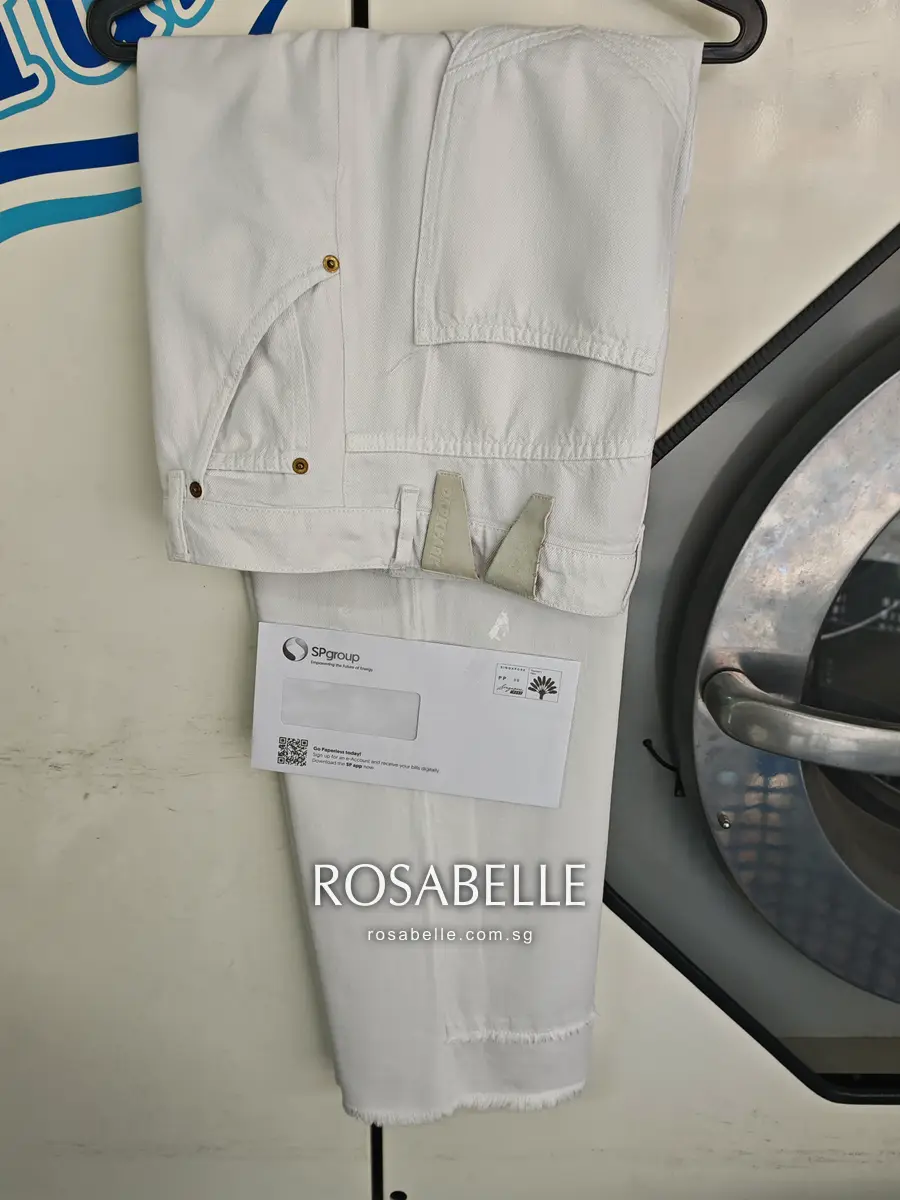 Cleaned jeans folded over a hanger, white denim, brass rivets and the back patch showing, a white envelope beneath
