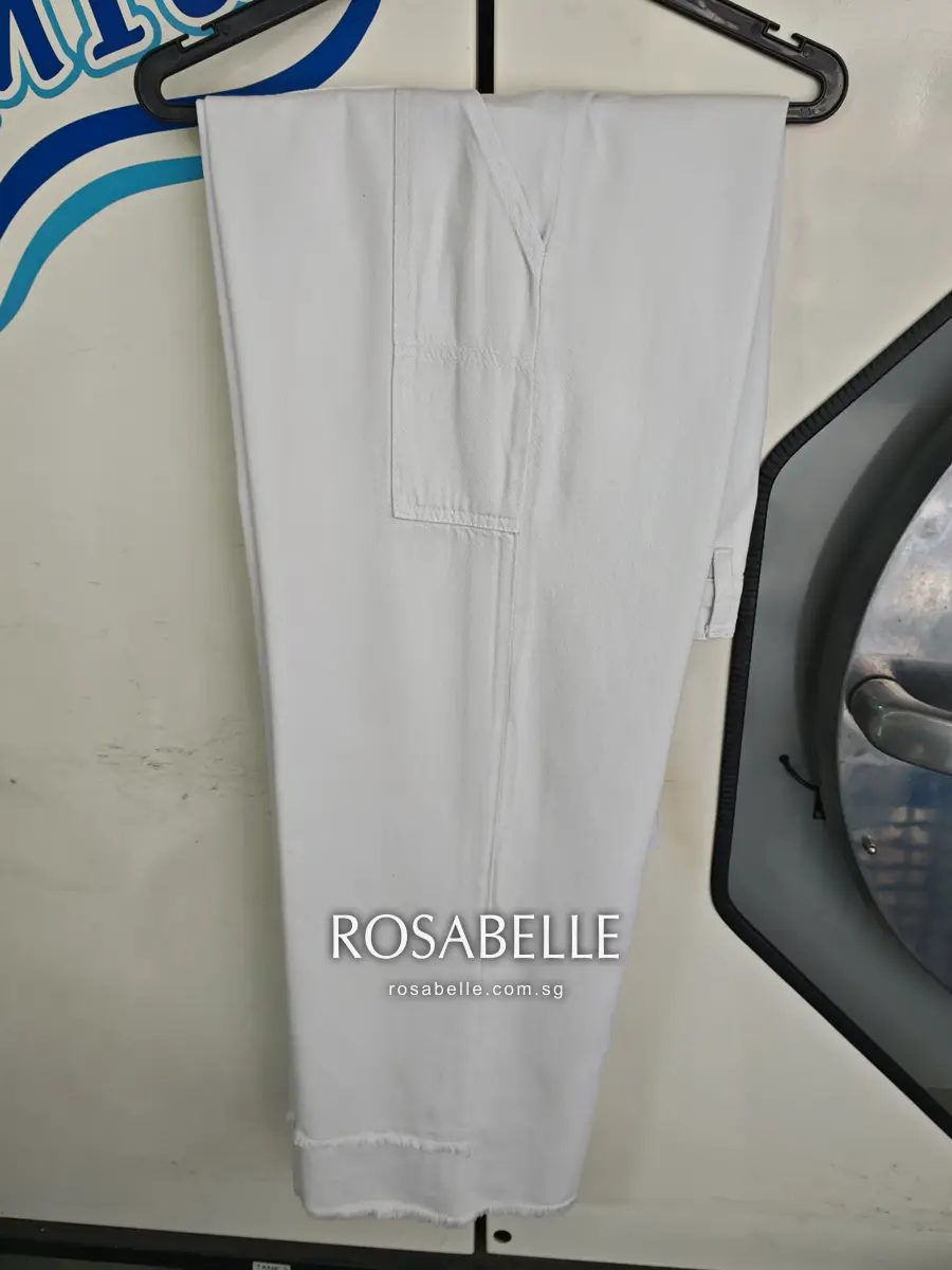 The same jeans folded lengthways on a hanger after cleaning, white from waistband to raw hem, front pocket seam visible