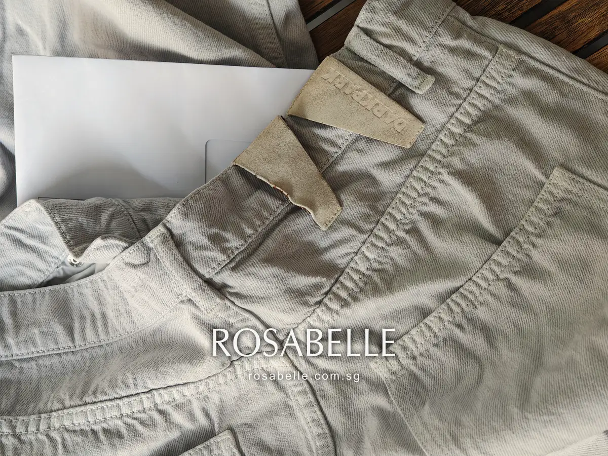 Back yoke and pocket of the grey jeans with the patch at the waistband, a white envelope at the top of the frame