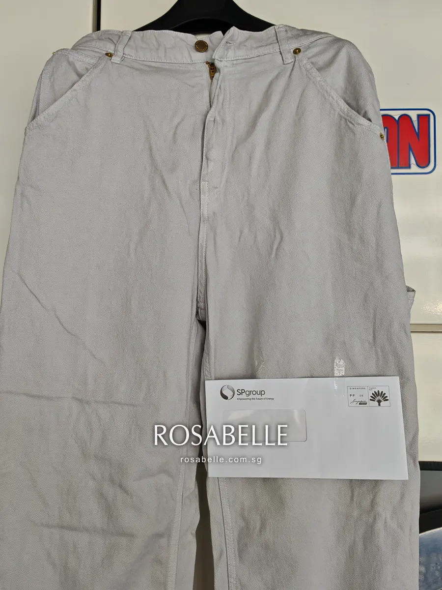 Upper half of the grey jeans with brass rivets at the pockets and a white SP group envelope across the thigh