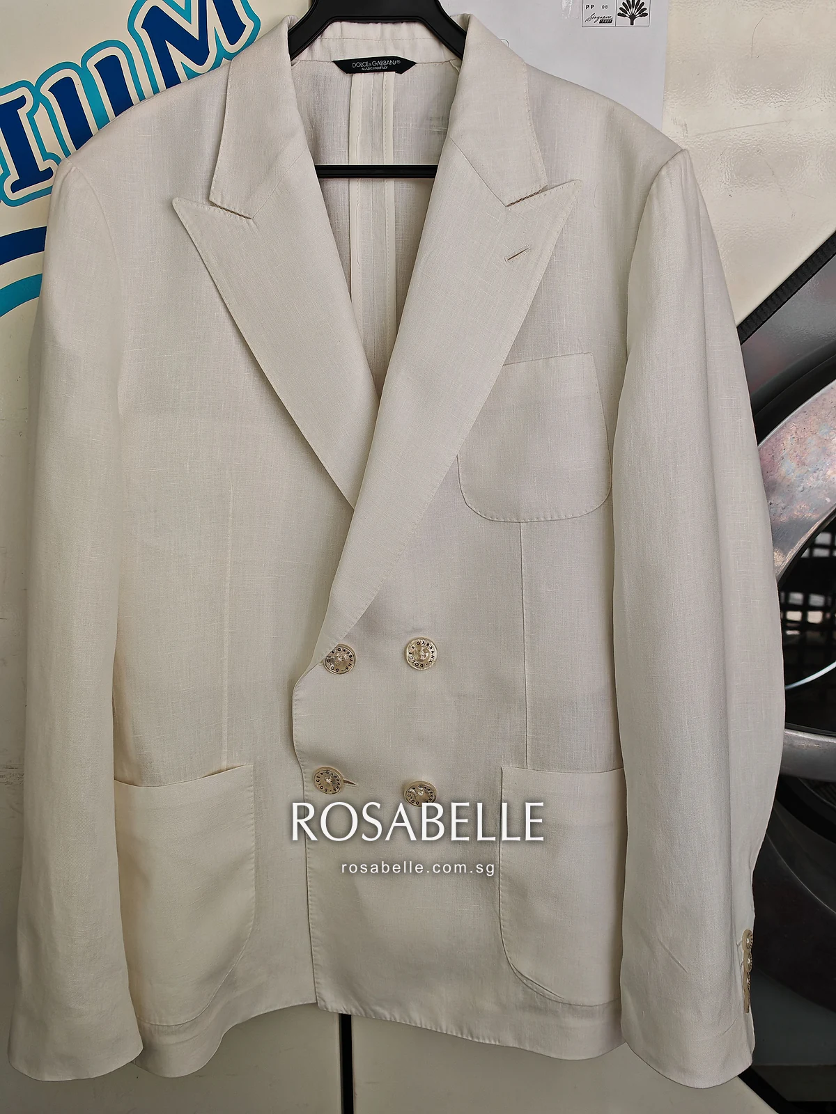 The same cream linen coat after cleaning, hanging buttoned with its logo buttons and patch pockets in view