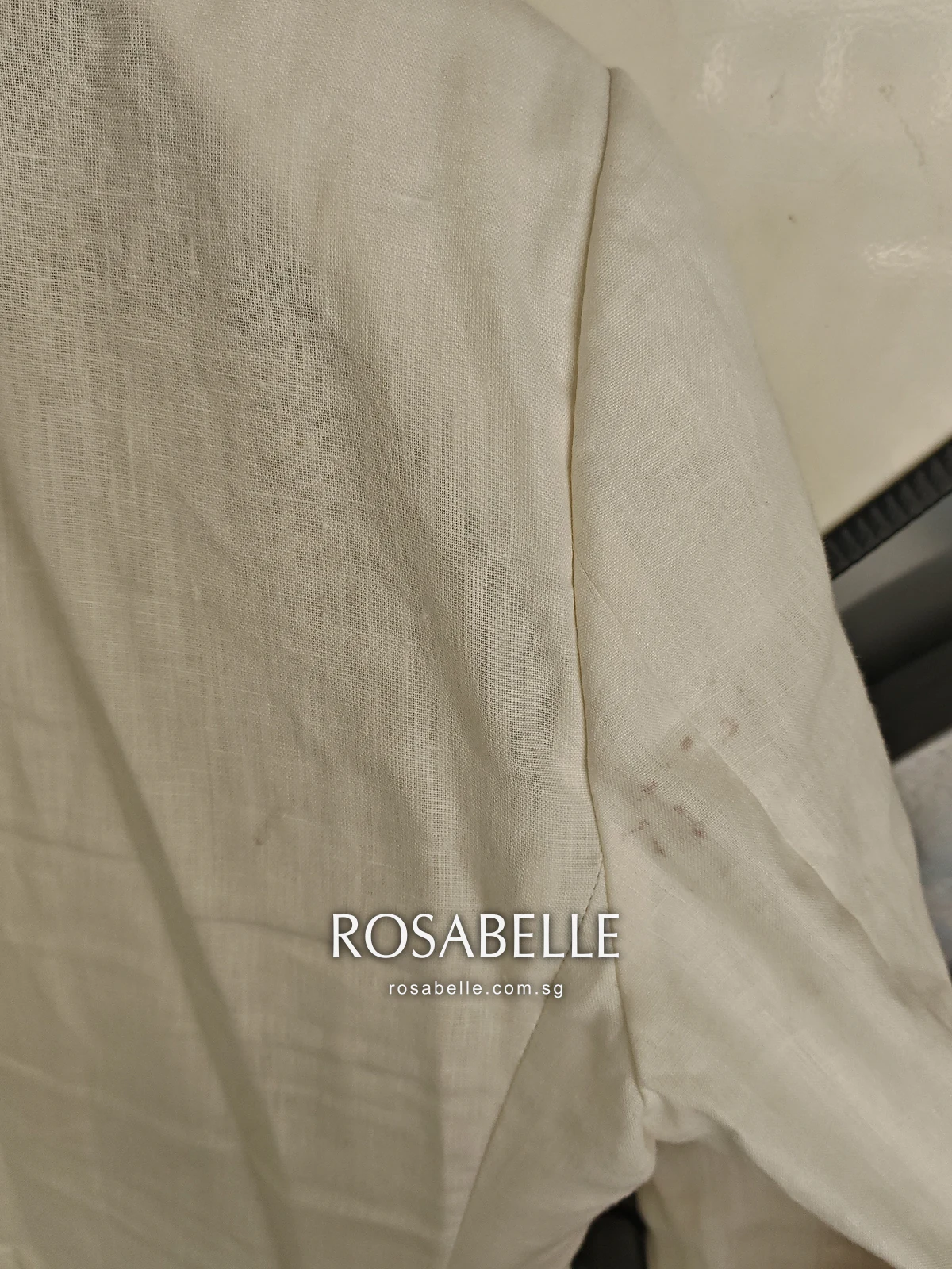 Sleeve of the cream linen coat before cleaning, a cluster of small reddish-brown wine spots on the slubbed weave