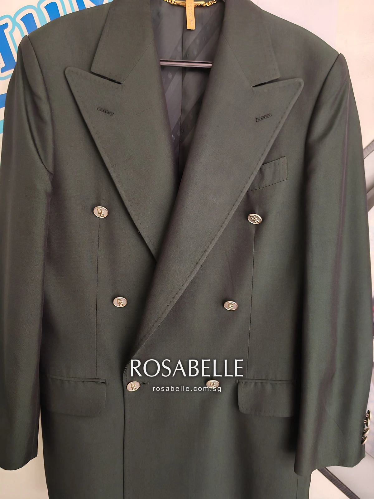 The same green silk coat after cleaning, hanging against a white wall with its double row of buttons in view