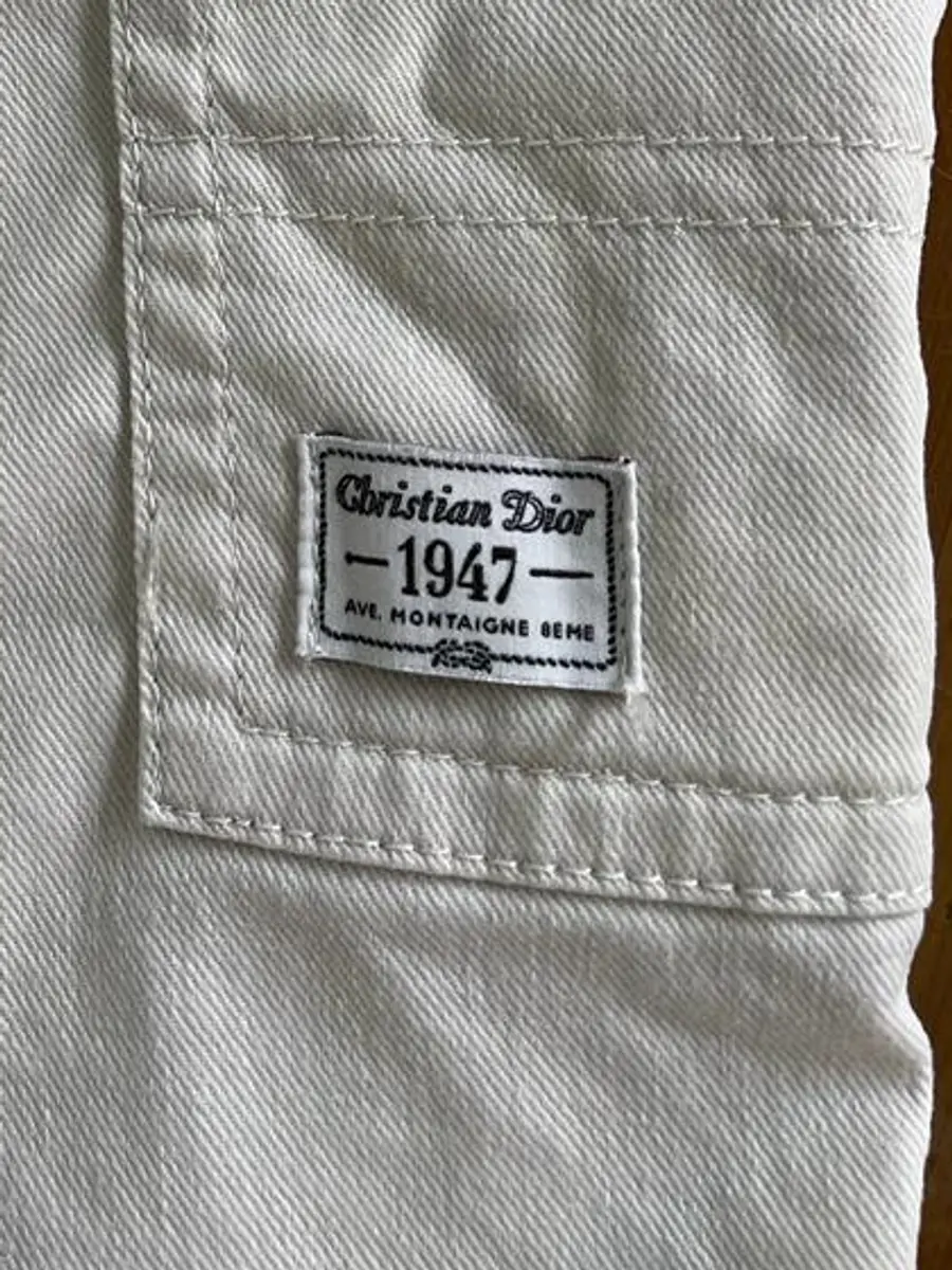 Woven label reading Christian Dior 1947 Ave. Montaigne 8eme stitched to the pocket of the cream cotton twill Bermuda shorts