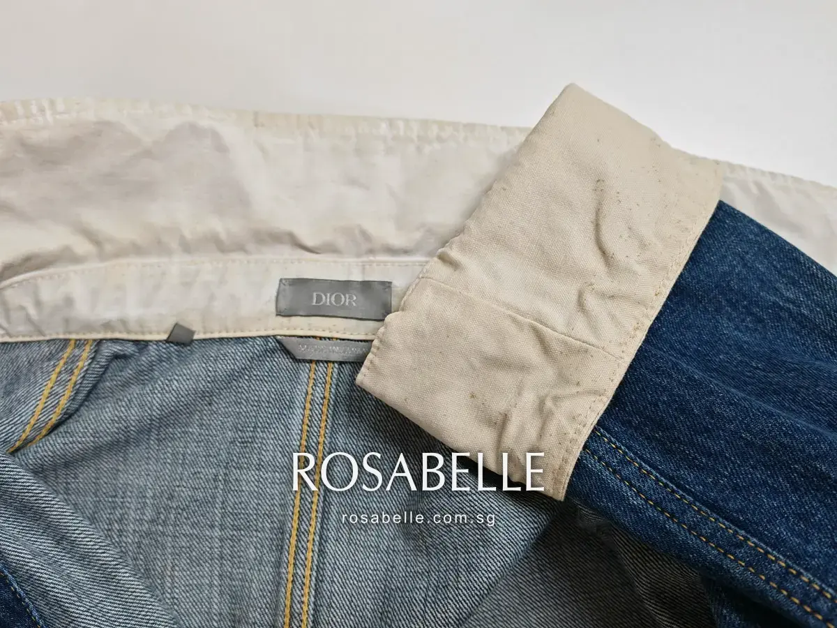Close view of the cream cotton collar band and turned-back cuff of a Dior denim jacket before cleaning, showing yellowing and fine brown speckling on the cuff