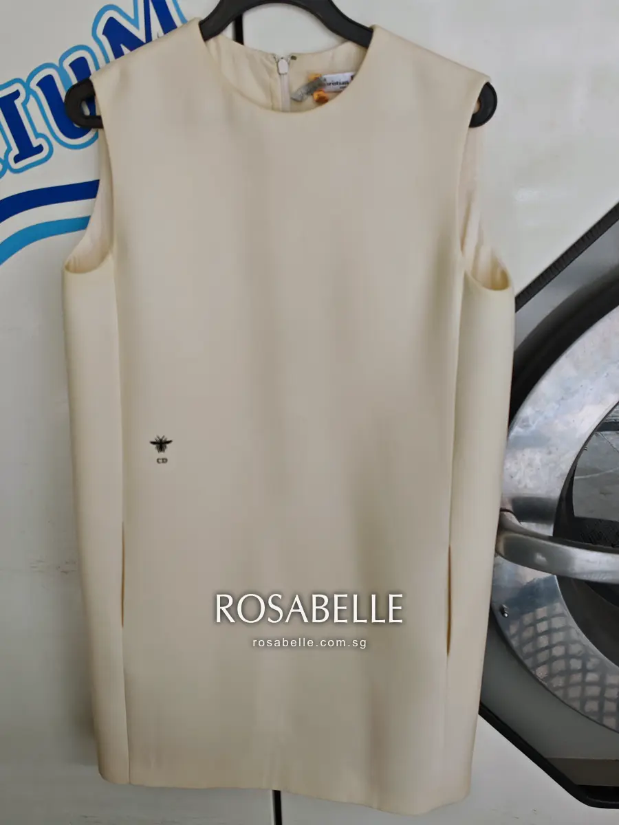 The same Dior dress after cleaning, shown from the front on a hanger with the embroidered CD bee below the bust