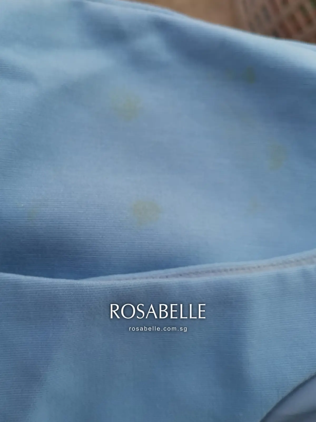 Close-up of yellow perspiration staining on pale blue fabric near the armhole before treatment