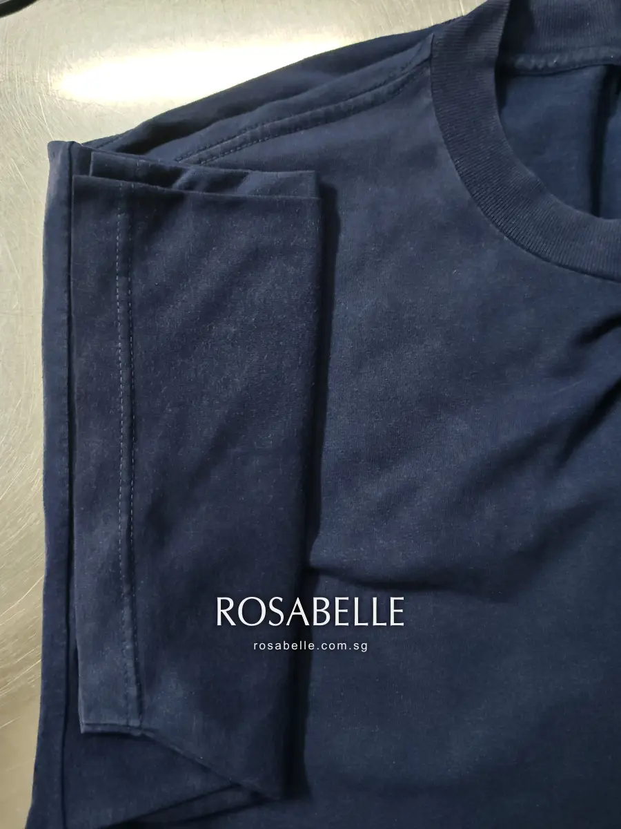 The same navy T-shirt sleeve folded on a steel table after cleaning, jersey clear of glue beside the crew neck