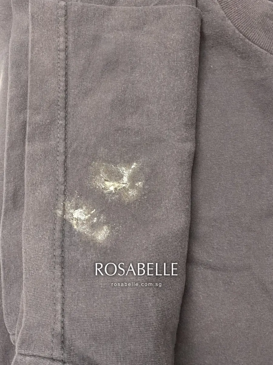 Folded sleeve of a navy cotton jersey T-shirt with two chalky white patches of dried glue near the hem stitching