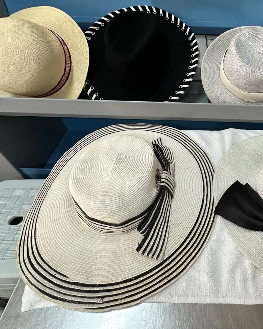 A collection of designer hats at Rosabelle Launderette Singapore — cream straw boaters, a black felt hat with whipstitched brim, and wide-brimmed straw hats with striped bands