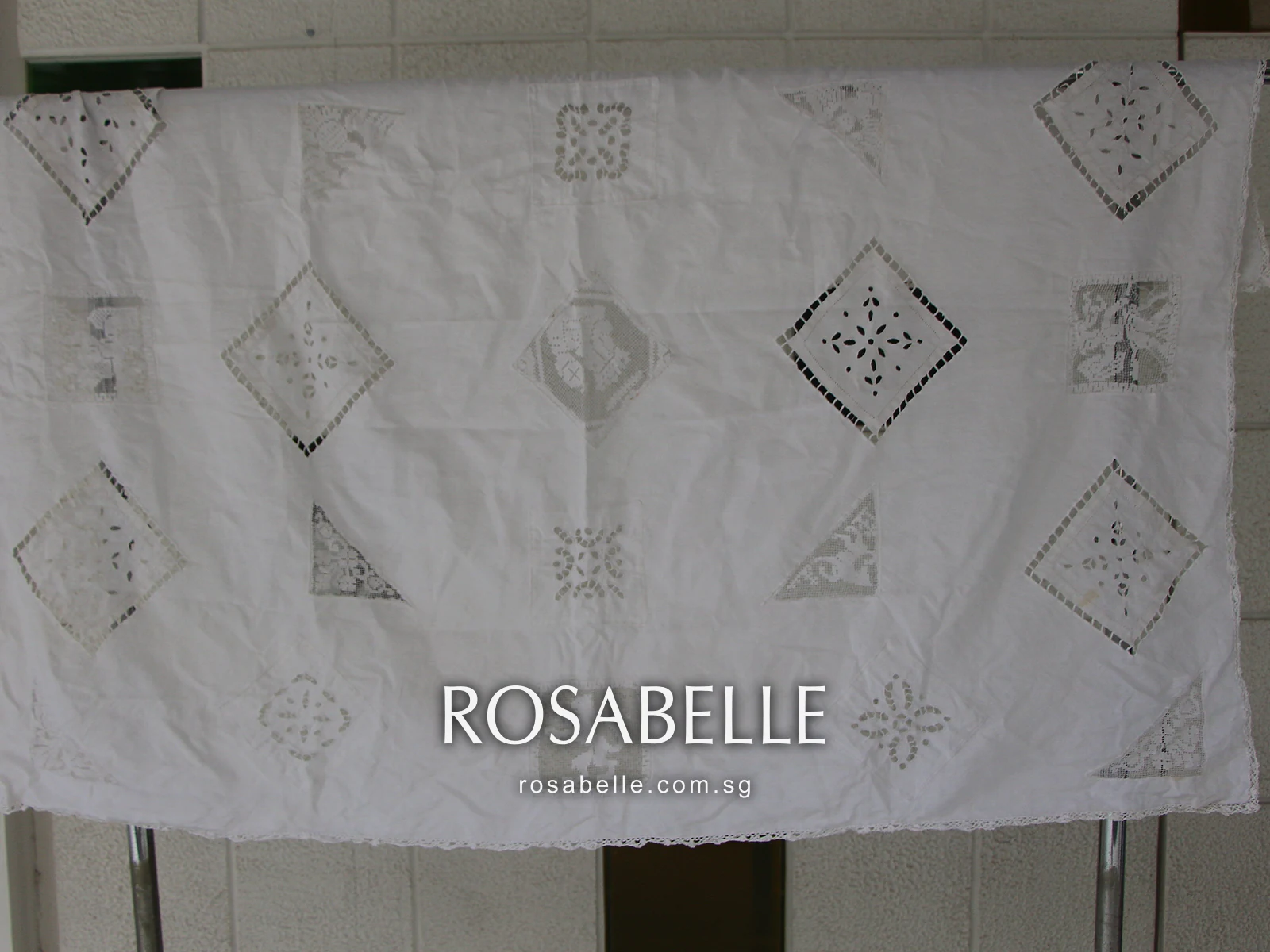 The same cutwork tablecloth folded over the rack after cleaning, its linen even and the lace insets clear