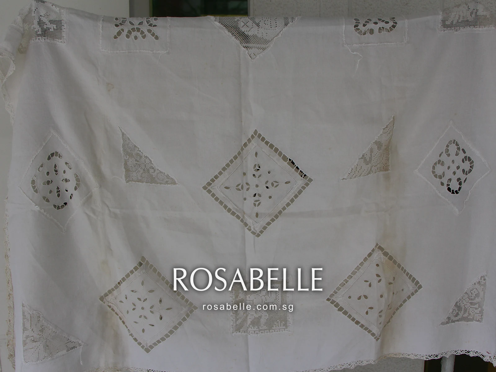 Cutwork tablecloth turned on the rack before cleaning, faint brown patches around the central open diamond