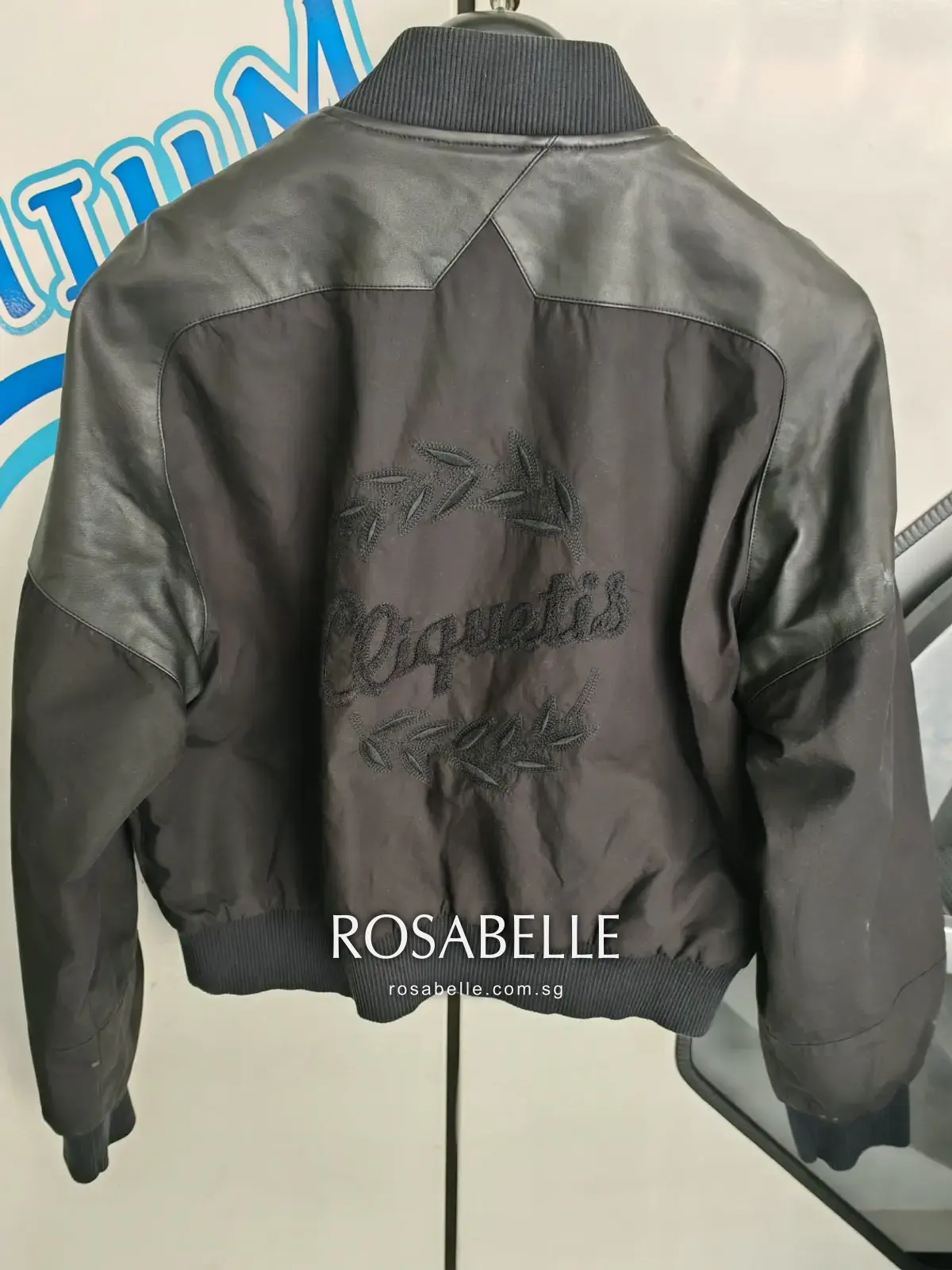 Back of the Hermès bomber jacket showing the embroidered script and laurel on the cotton panel between lambskin shoulders