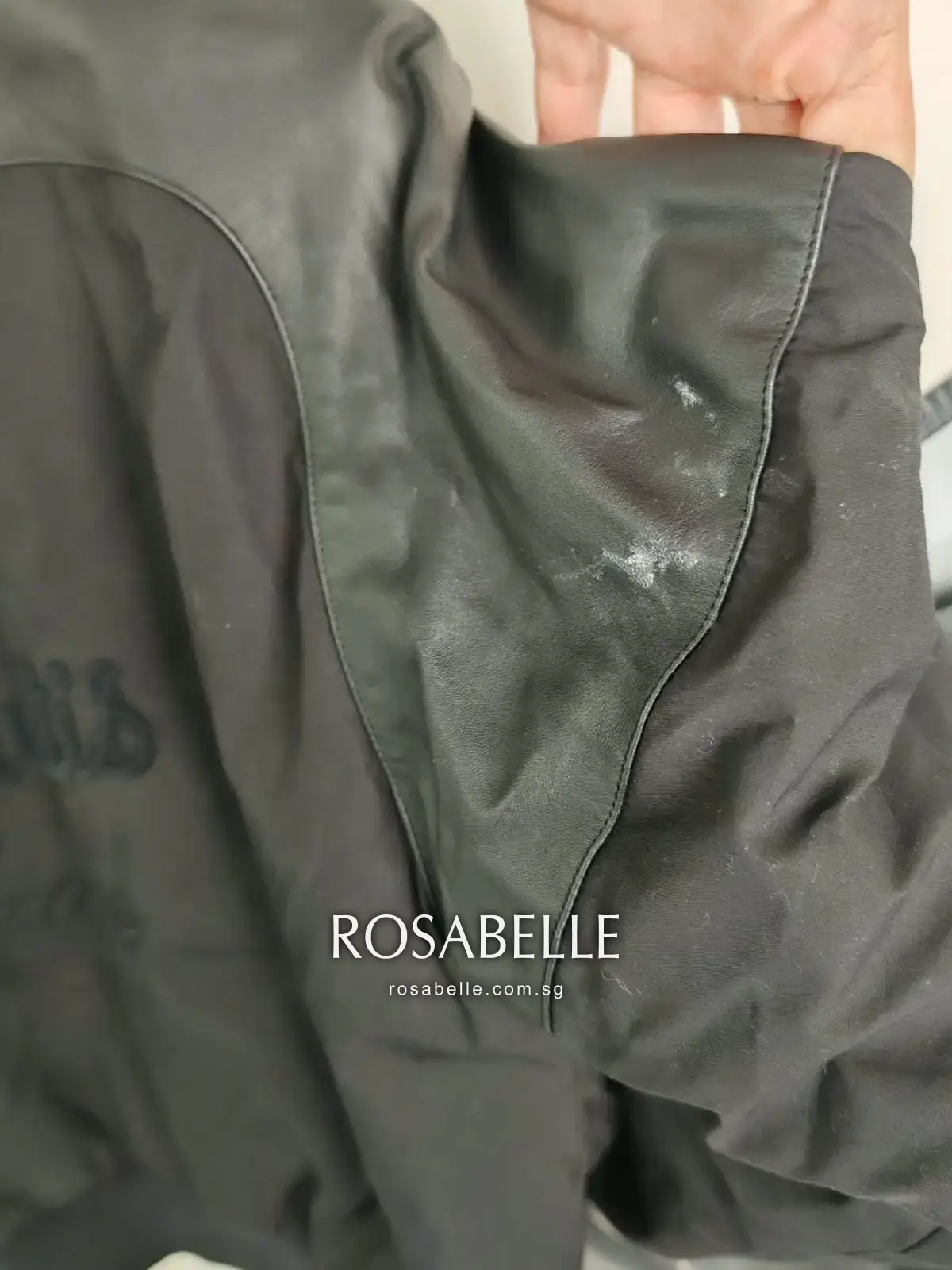 Close-up of the Hermès bomber jacket where the lambskin sleeve panel meets the cotton body, with white marks on the leather before cleaning