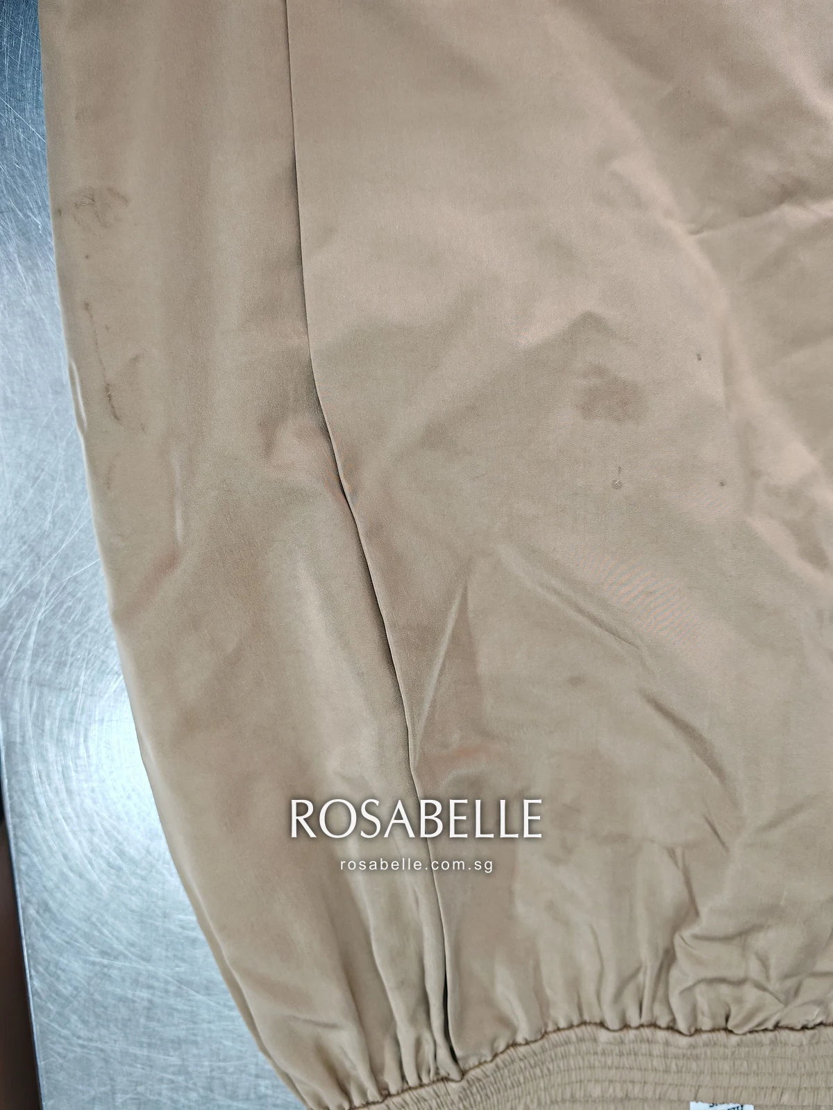 Close view of the camel silk before cleaning, several irregular darker food spots near a gathered edge
