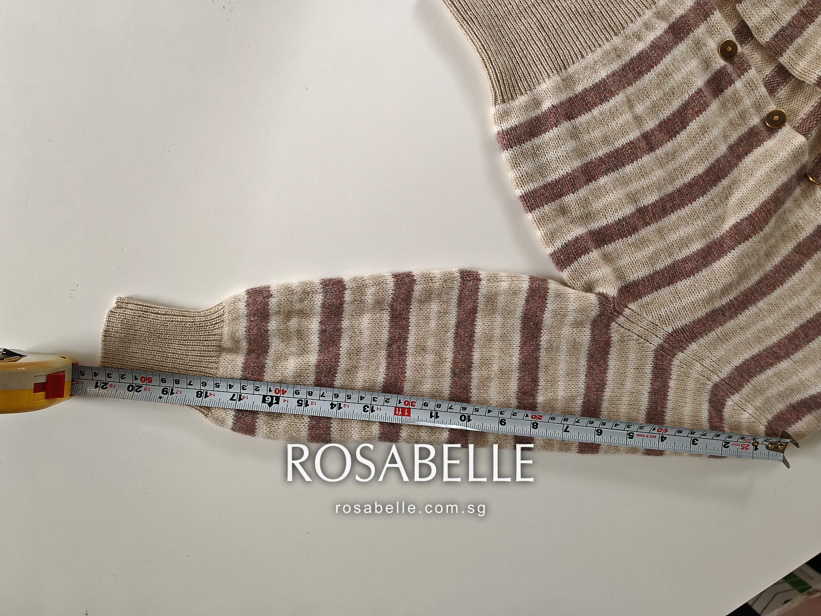 One striped cashmere sleeve stretched along a tape from shoulder seam to ribbed cuff, the body of the cardigan above it
