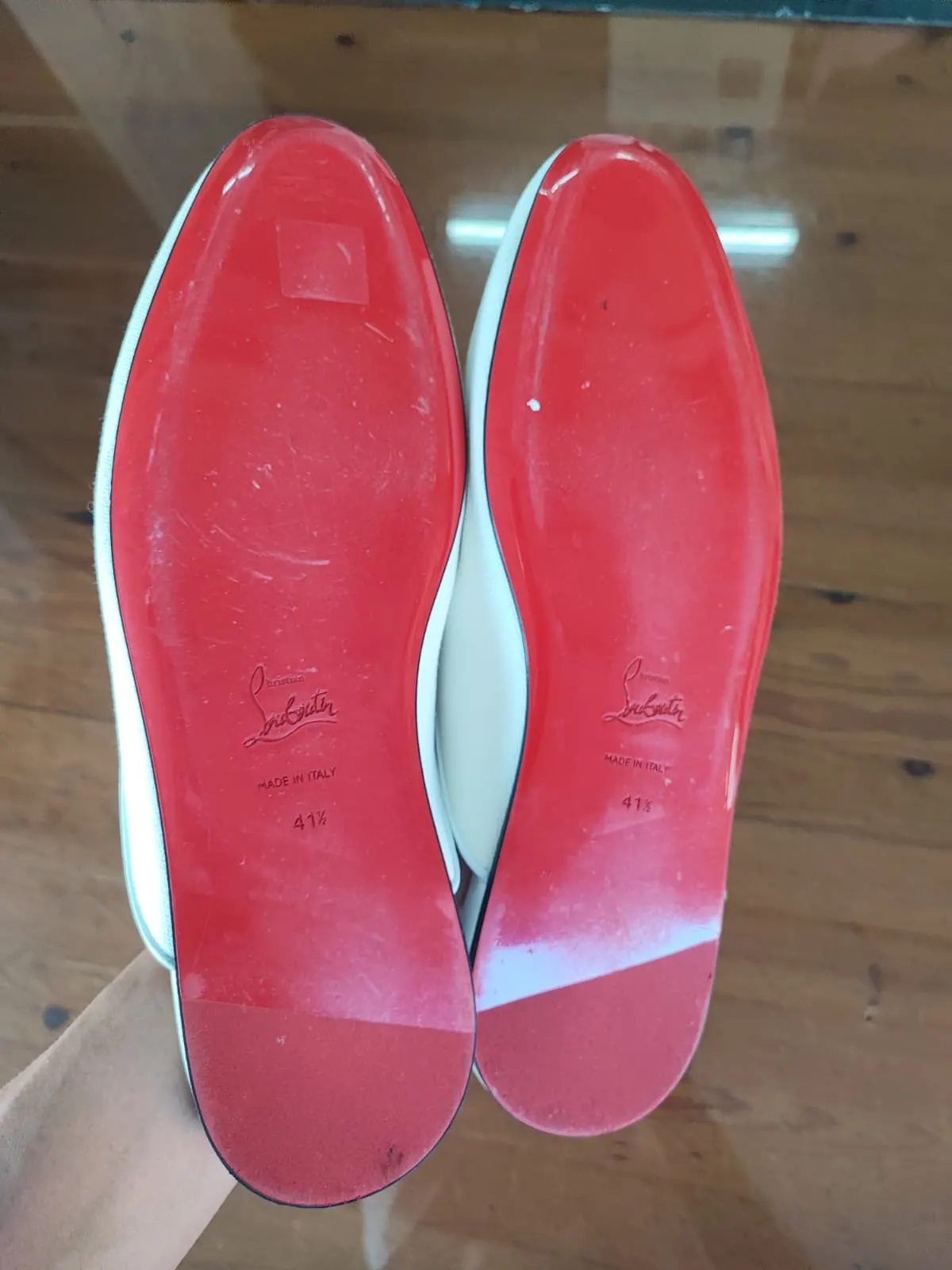 Red lacquer soles of the Louboutin mules dulled by sticker residue and street film before cleaning