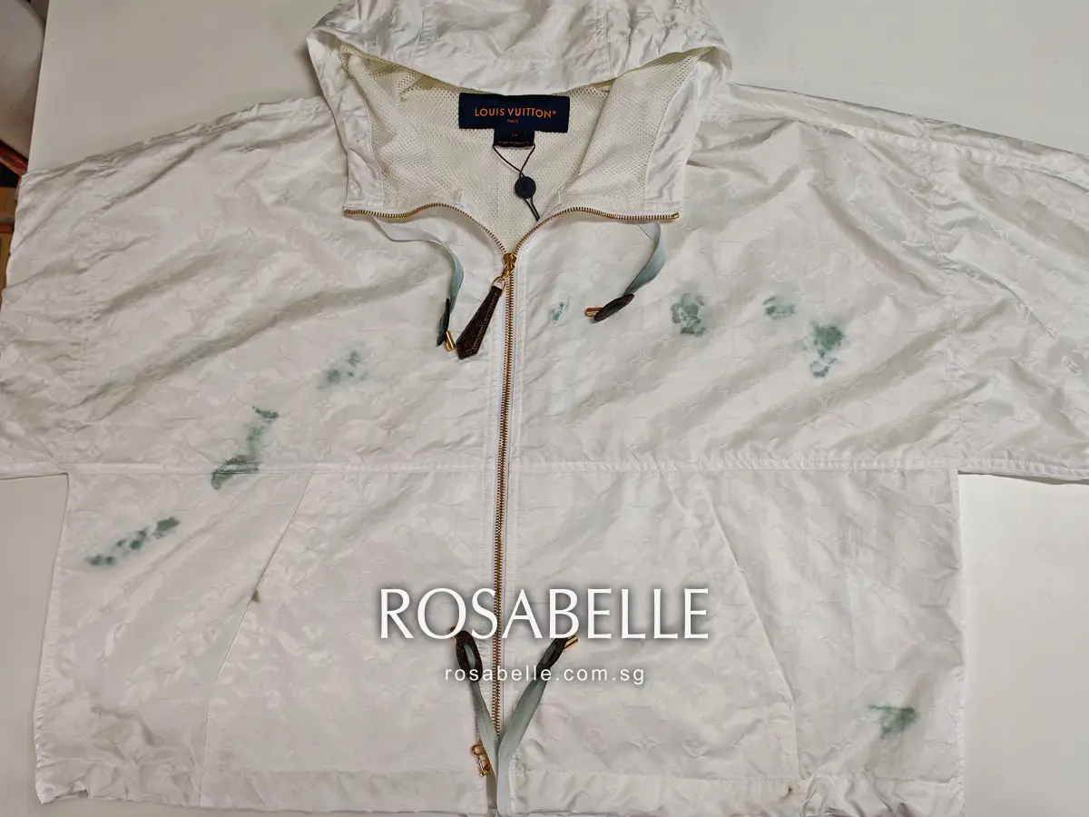 White Louis Vuitton hooded parka laid flat before cleaning, bluish-green dye blotches across the front and teal-tinted cords