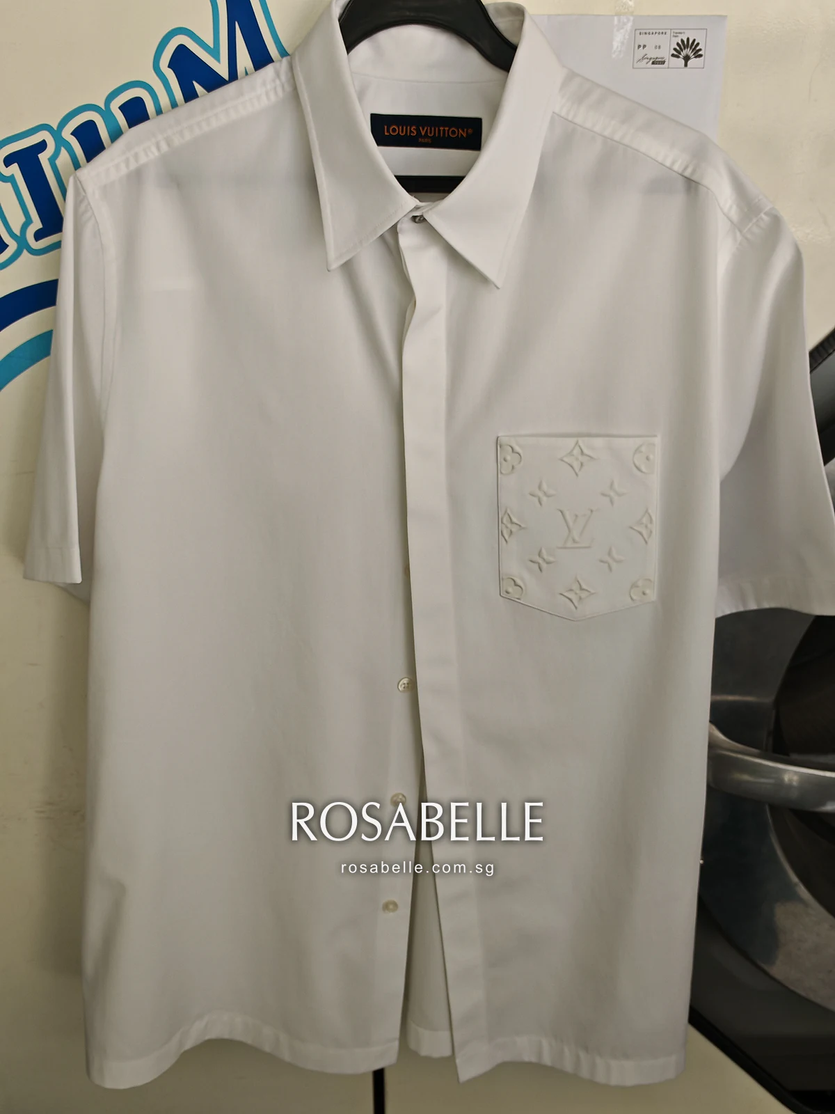 The same white Louis Vuitton shirt after cleaning, hanging with the collar open and the monogram pocket in view
