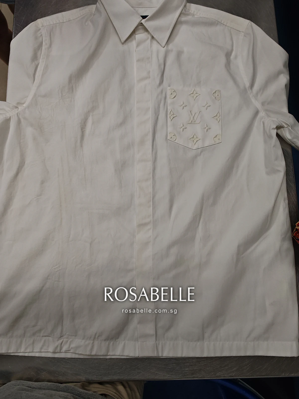 White Louis Vuitton short-sleeve shirt laid flat, embossed monogram patch pocket on the chest, before colour run removal