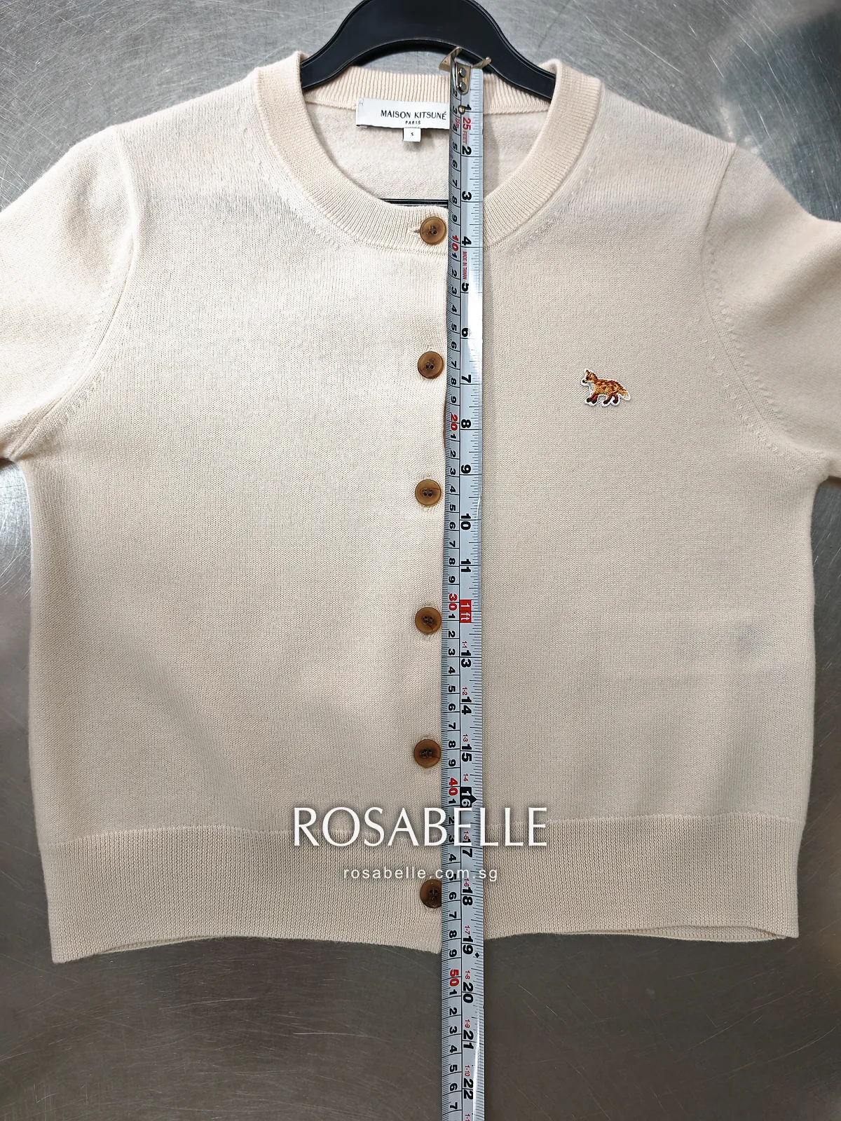 The same fox-patch cardigan after reblocking, on a hanger over the table with the tape running the full length of the front