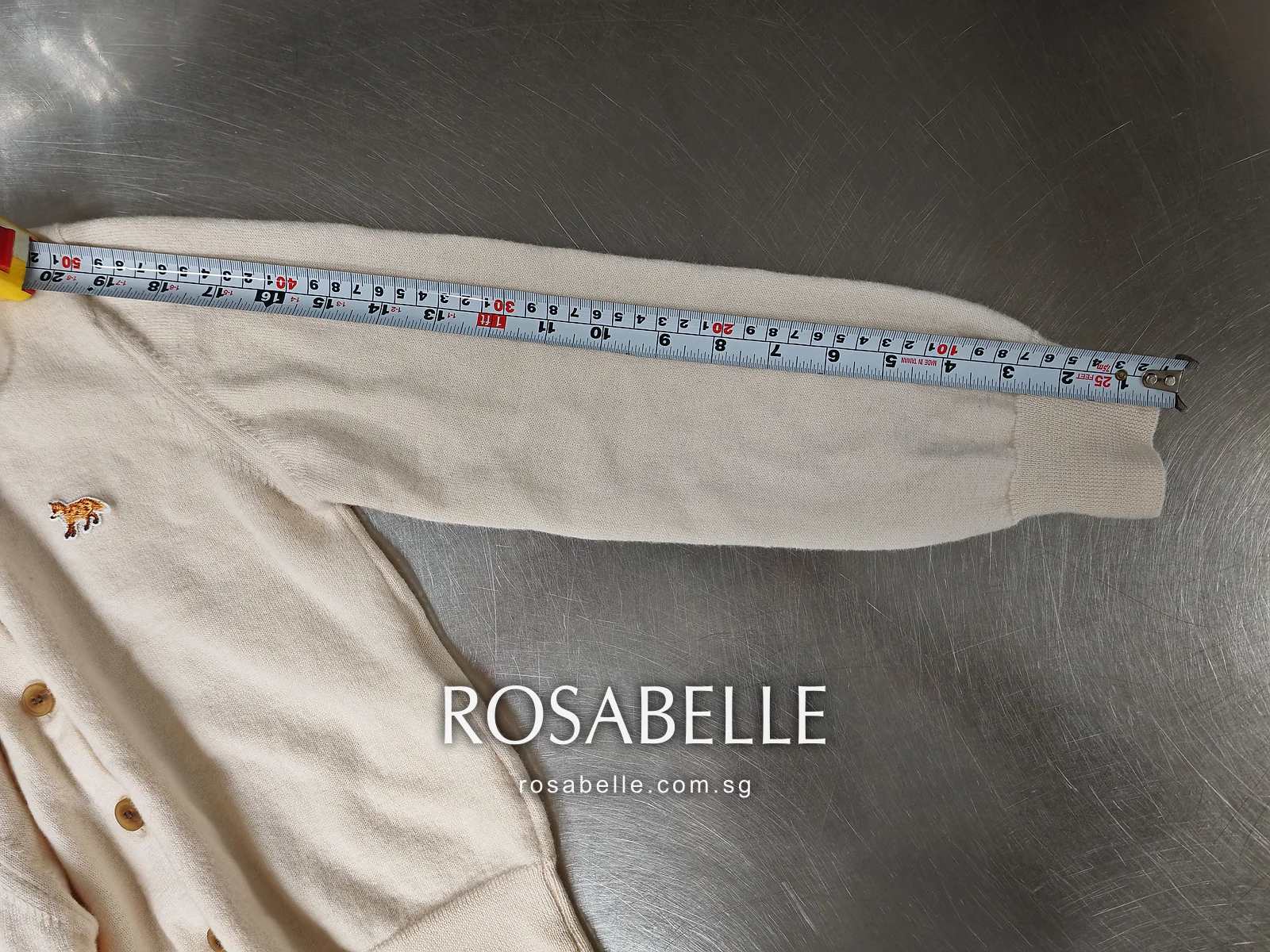 One sleeve of the merino cardigan stretched along a tape from shoulder seam to ribbed cuff before reblocking