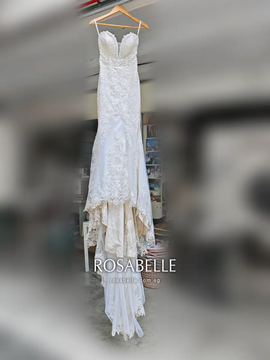 Ivory lace mermaid wedding gown on a wooden hanger, fitted to the knee, with a darkened underskirt showing beneath the flare