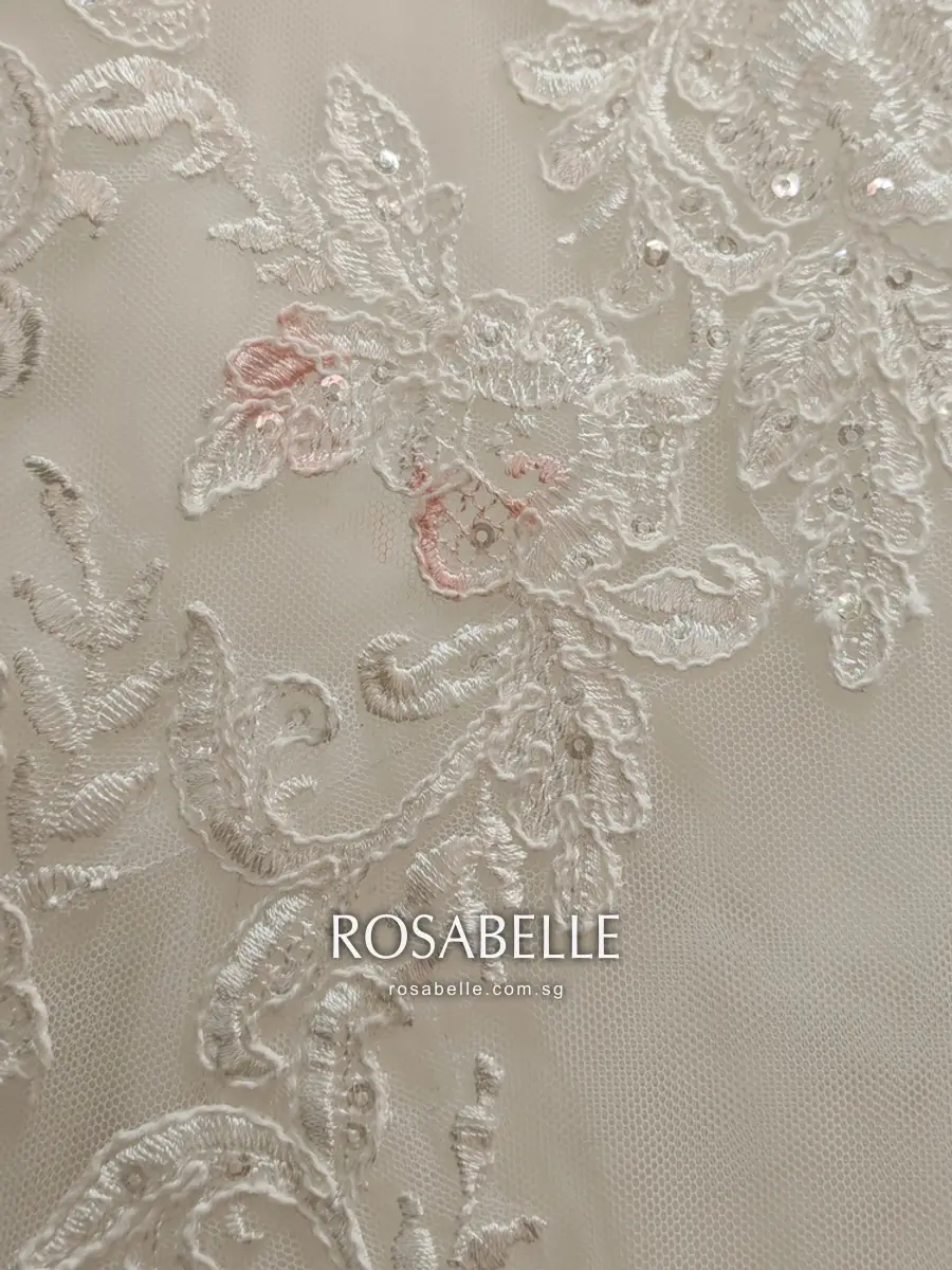 Close view of sequinned lace appliqués on tulle, two of the flower motifs tinted pink by a makeup-like mark