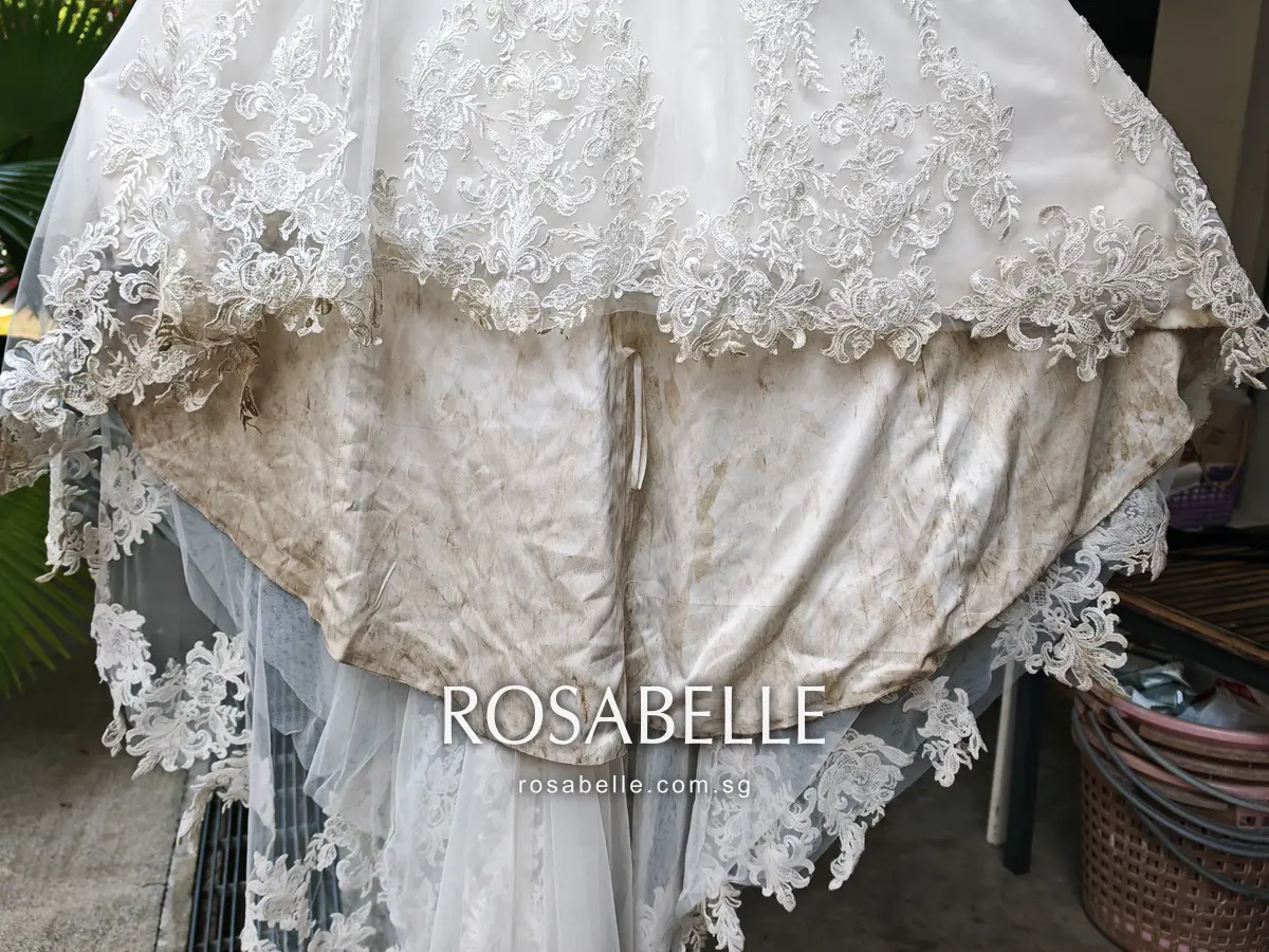 Underside of the gown flare showing a satin underskirt streaked grey-brown, with lace-edged tulle hanging beneath it
