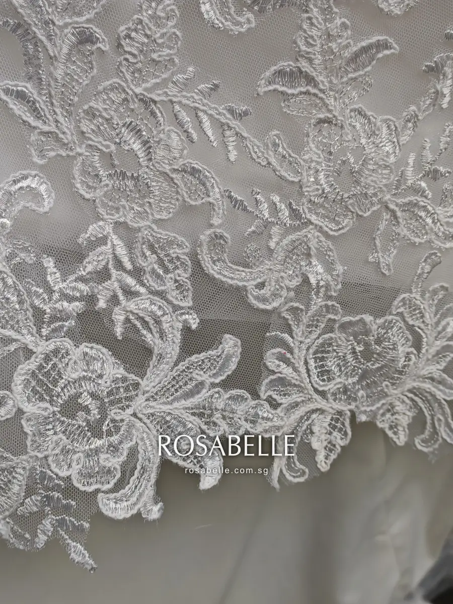 Close view of the scalloped lace edge of the skirt, embroidered flowers and leaves outlined in raised cord