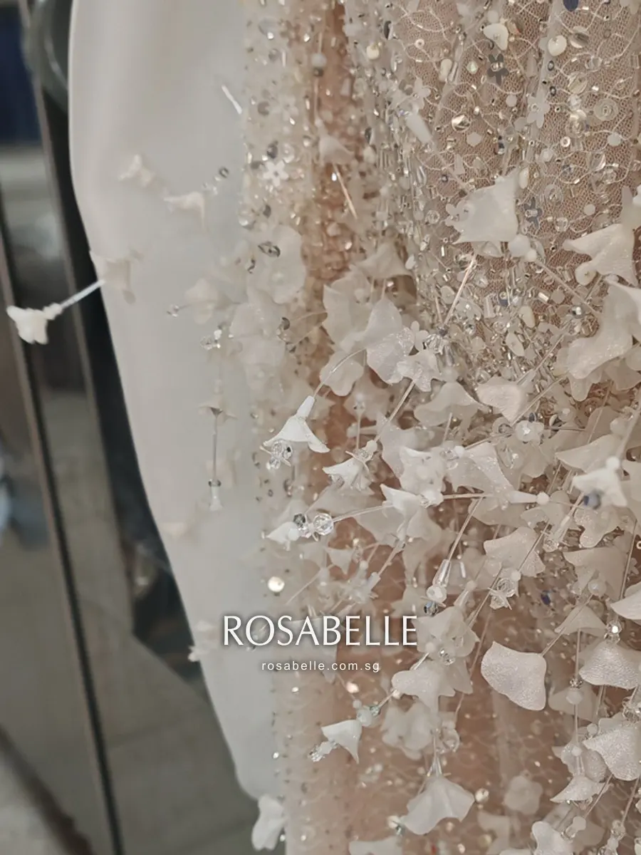 Close view of a blush beaded panel scattered with three-dimensional white fabric petals and small sequins