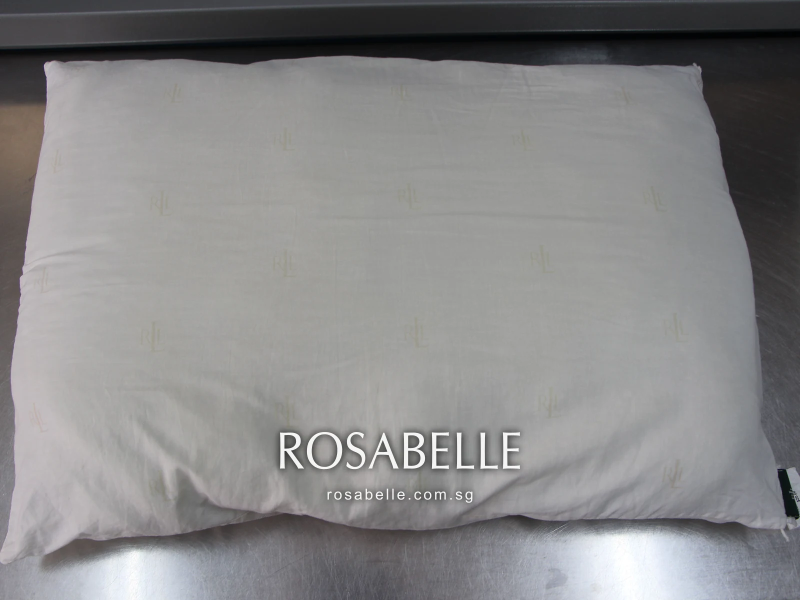 The same style of pillow with its dark corner tag, clean and even in colour on a steel work table