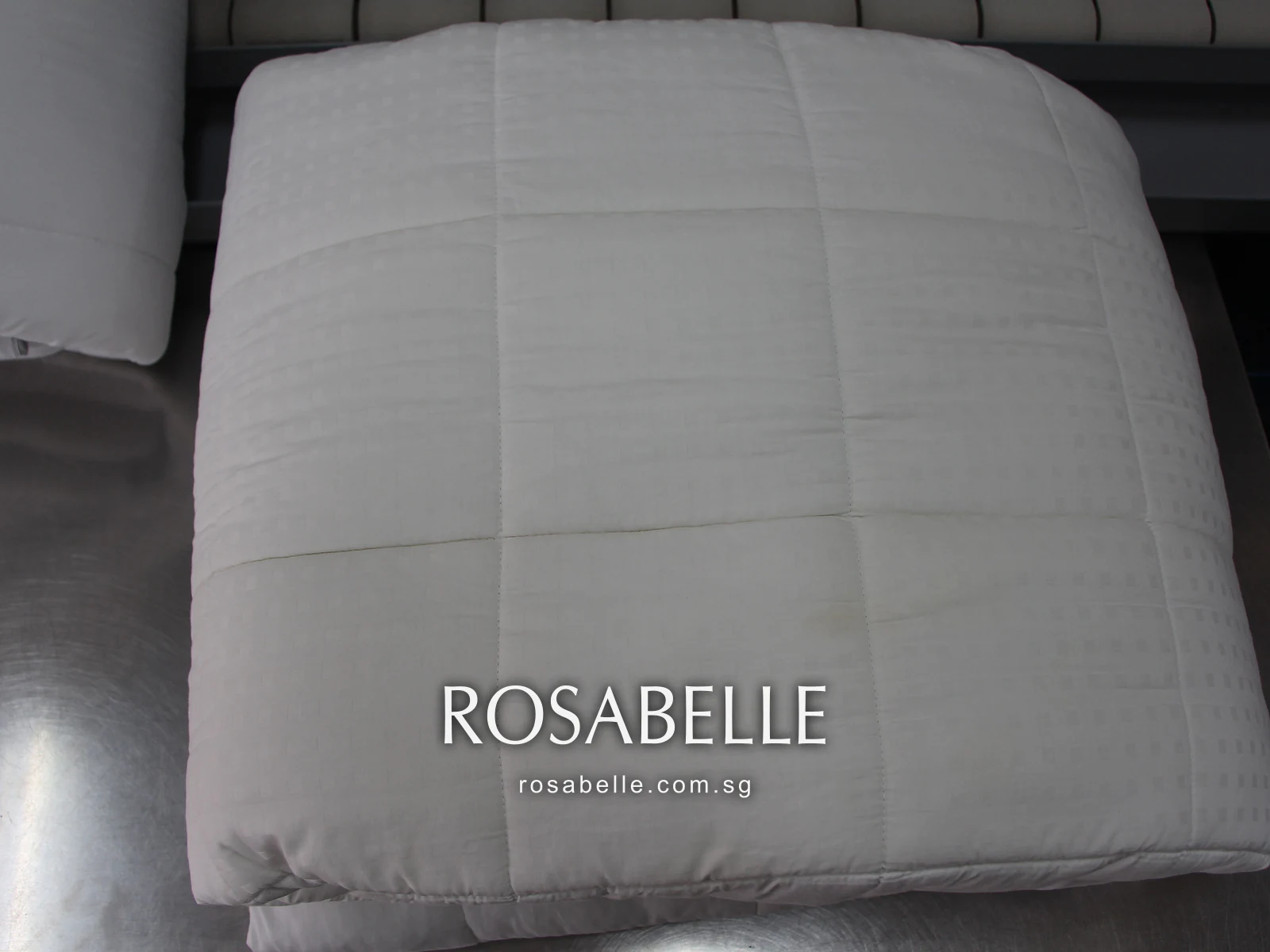 Square-quilted white duvet folded on a steel table after cleaning, its stitch lines clear
