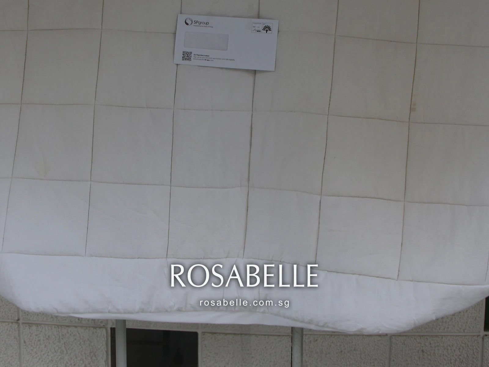 Lower panels of a white square-quilted duvet hanging against a tiled wall, brown marks along the stitching