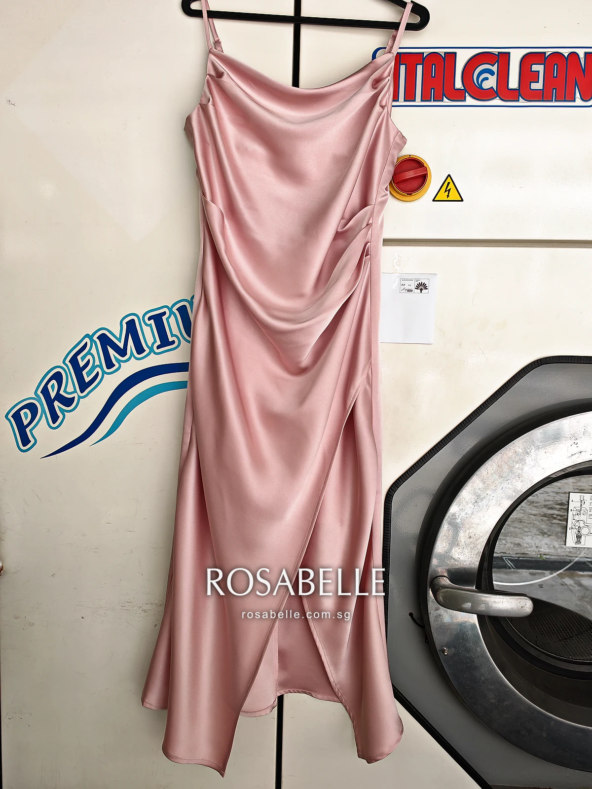 Pink satin slip dress with a cowl neck and thin straps on a hanger after cleaning, the draped skirt falling to a side slit