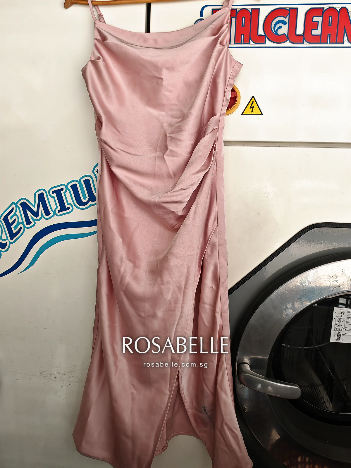 Pink satin slip dress on a hanger before cleaning, a dark eyeliner line on the lower skirt near the side slit