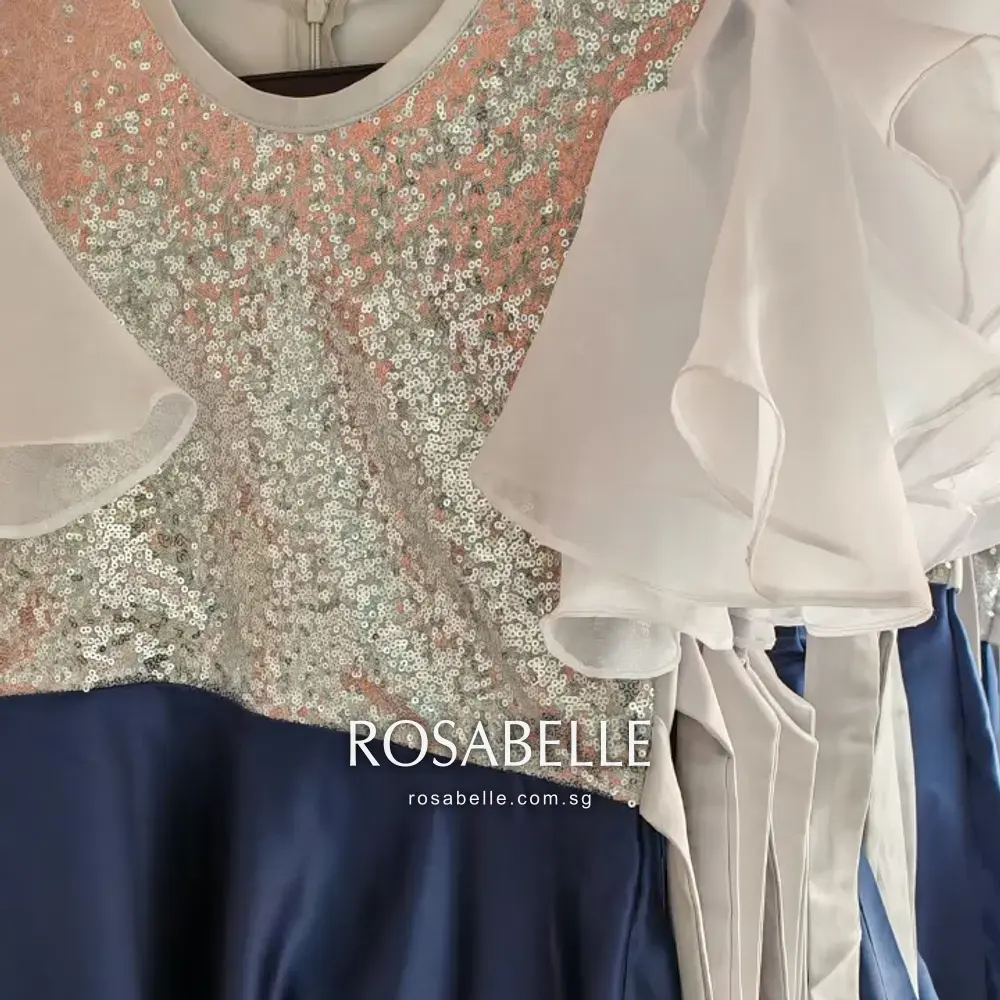 Close view of a school choir dress with a sequinned bodice, white organza flutter sleeves and a navy satin skirt, in for cleaning