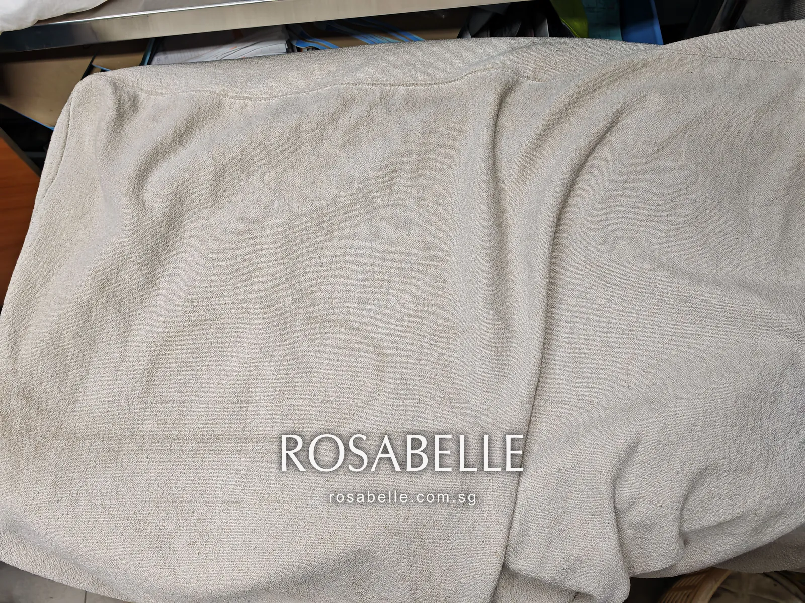 Cream cushion cover draped loosely, faint curved lines in the lower half where a spill dried into the pile