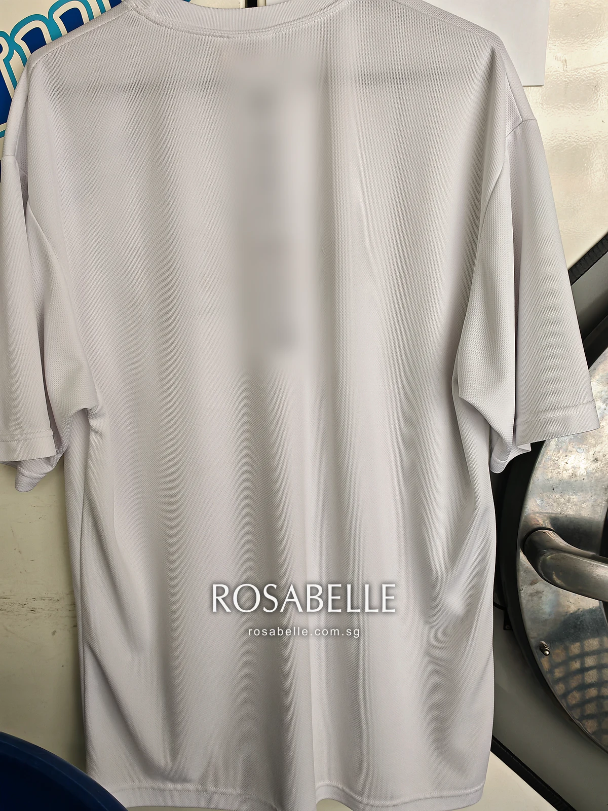 Back of the T-shirt hanging after cleaning, the mesh knit white with no marks across the shoulders or lower back