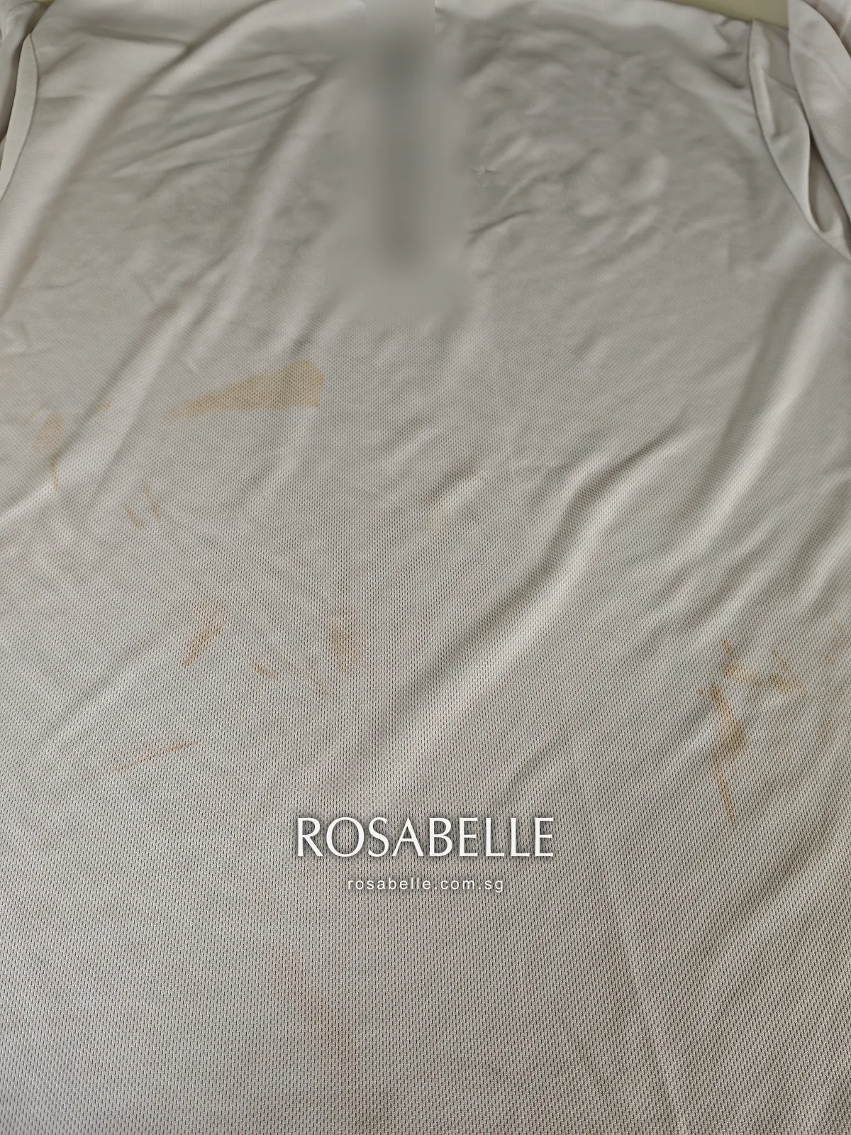 Back of the white polyester T-shirt laid flat, faint brown sunscreen marks scattered over the lower back