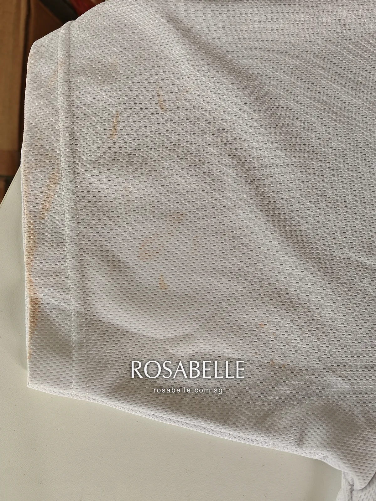 Close view of the open mesh knit near the hem, with brown sunscreen spots caught in the white polyester
